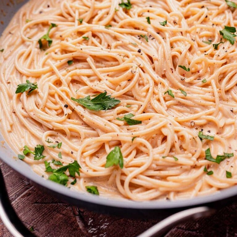 A pan of cooked spaghetti in a creamy coconut milk pasta sauce, garnished with chopped parsley and cracked black pepper.