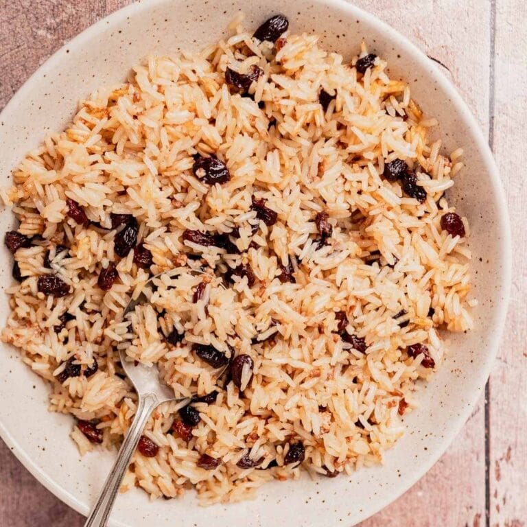 A plate of Arroz con Coco—cooked rice blended with raisins—is served with a spoon on a light-colored surface.