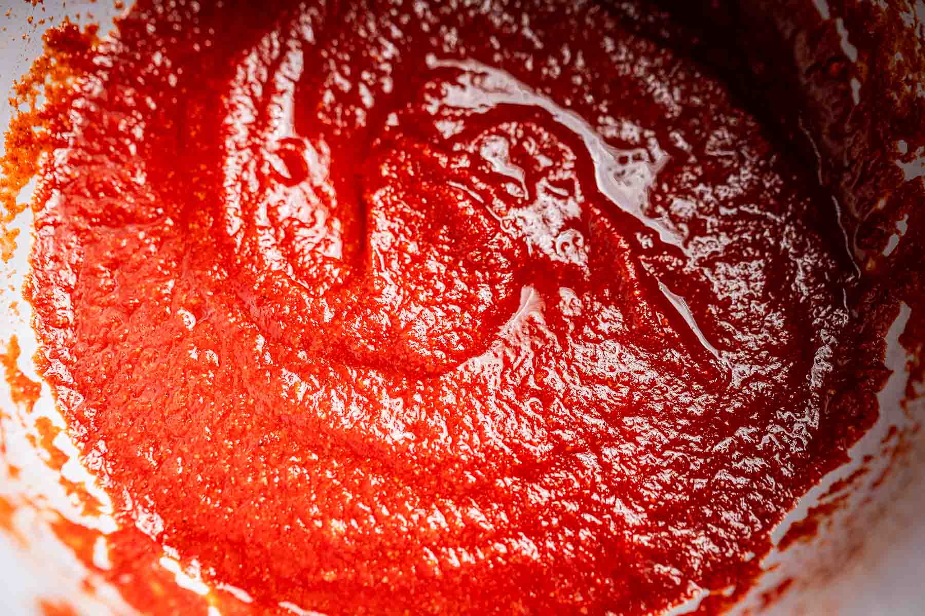 Close-up of a bowl filled with rich, red tomato paste, reminiscent of smooth taco sauce, showcasing a textured, glossy surface.