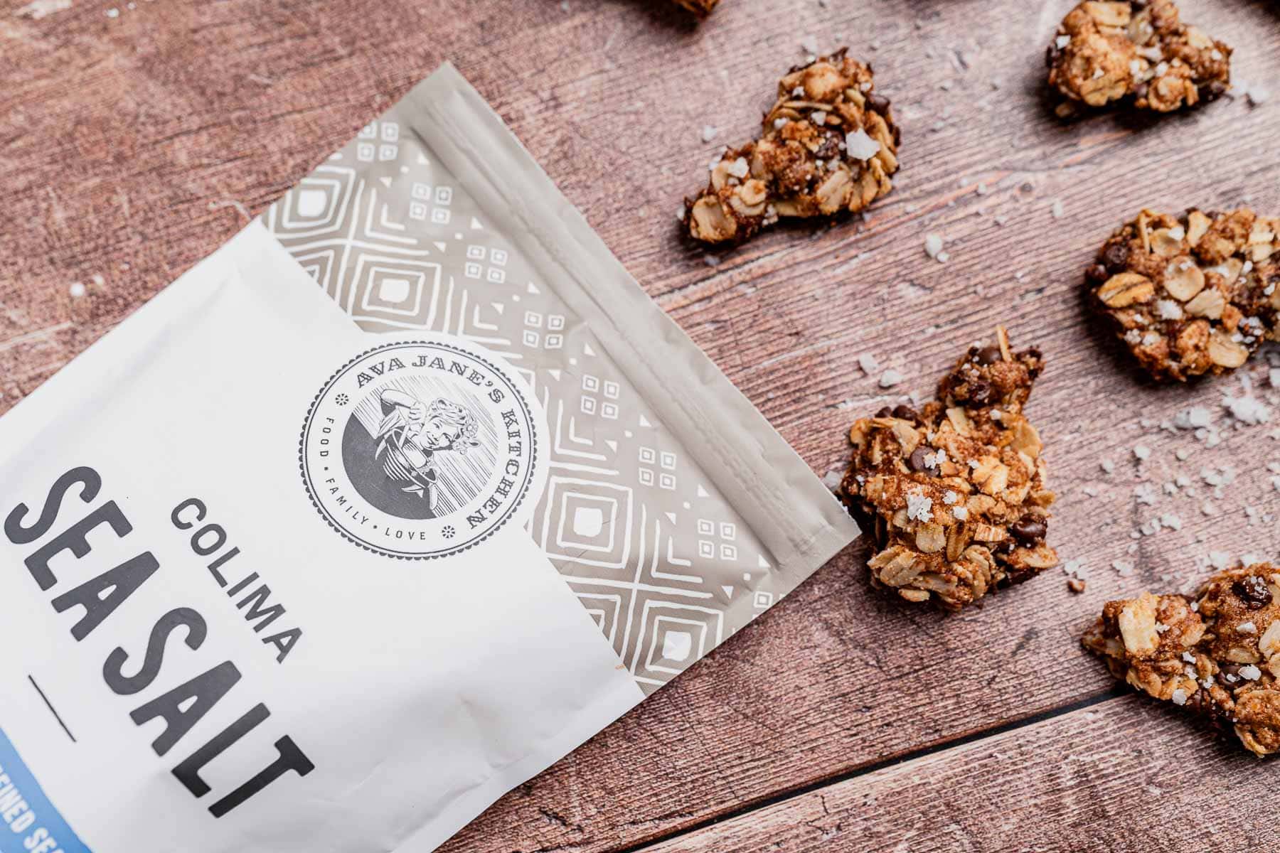 A package of Colima sea salt on a wooden surface next to clusters of chocolate chip cookie granola, each richly sprinkled with sea salt.