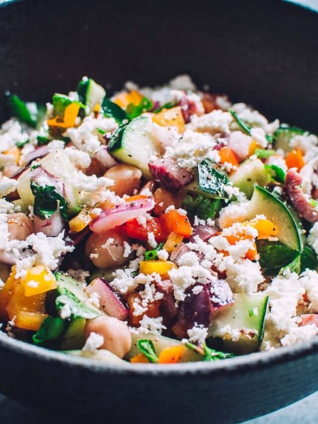 A bowl of chopped vegetables, chickpeas, herbs, and crumbled cheese mixed together.