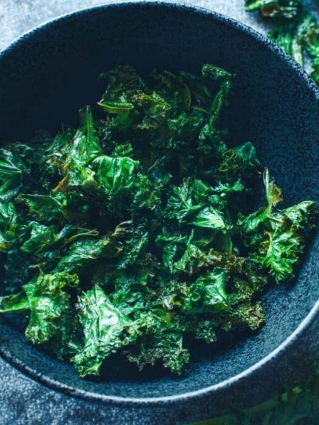 A black bowl filled with crispy baked kale chips on a dark textured surface.