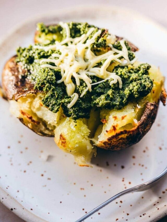 Baked potato on a white plate topped with green pesto and grated cheese, with a fork on the side.