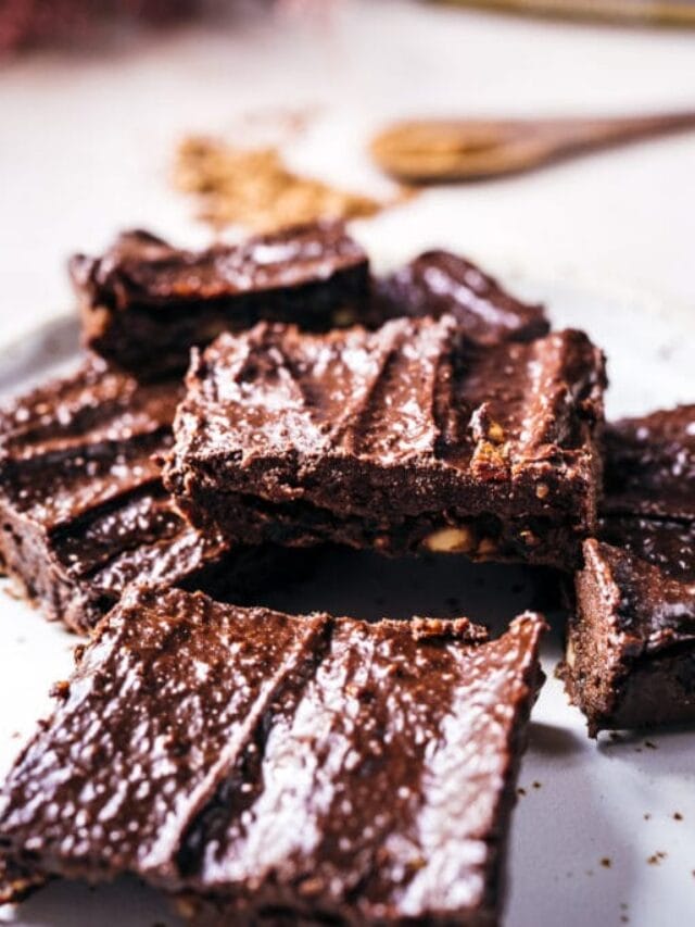 A plate of chocolate brownies with a glossy finish, arranged in a stack, set on a light-colored surface.