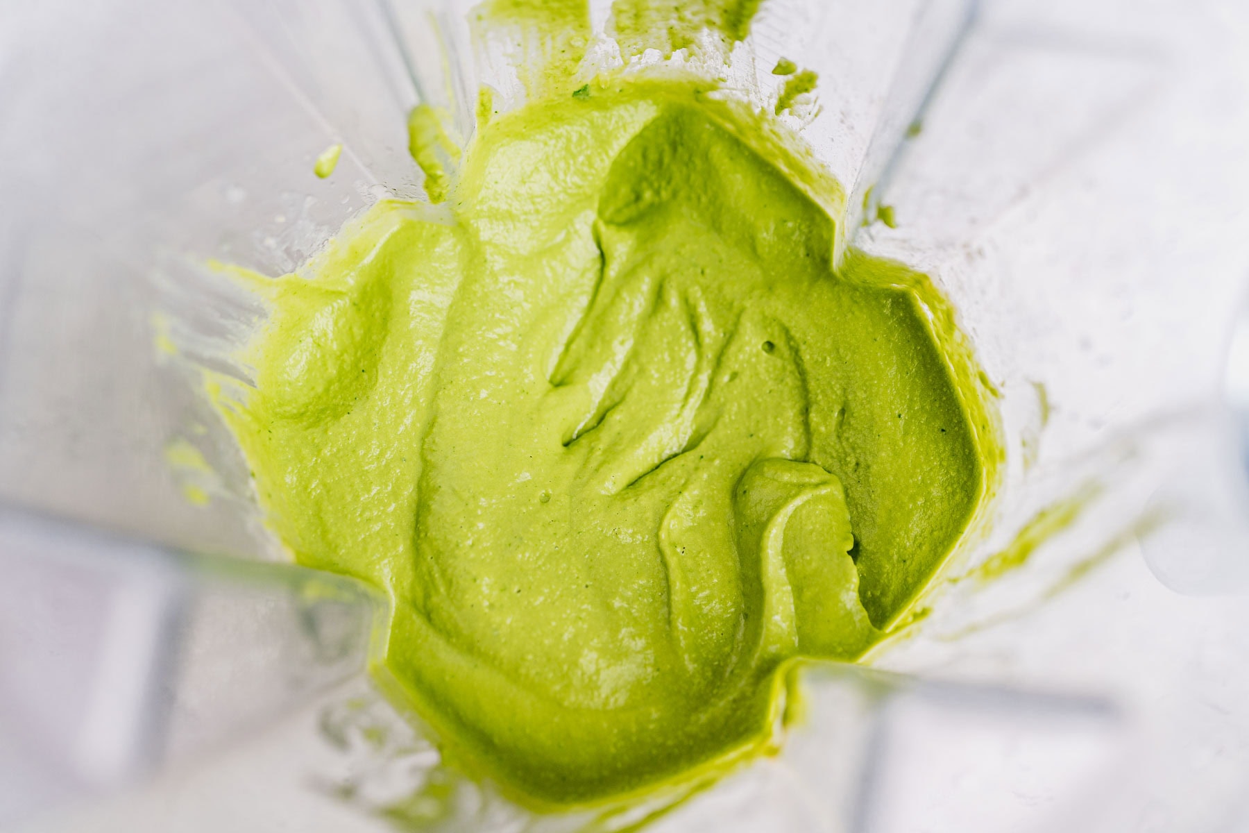 Bright green goddess hummus mixture inside a blender, with its creamy texture visible on the sides.