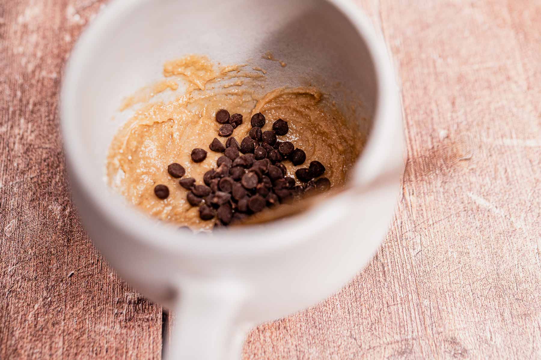 A bowl of cookie dough mixed with chocolate chips sits on a wooden surface, evoking the cozy simplicity of an oat flour mug cake.