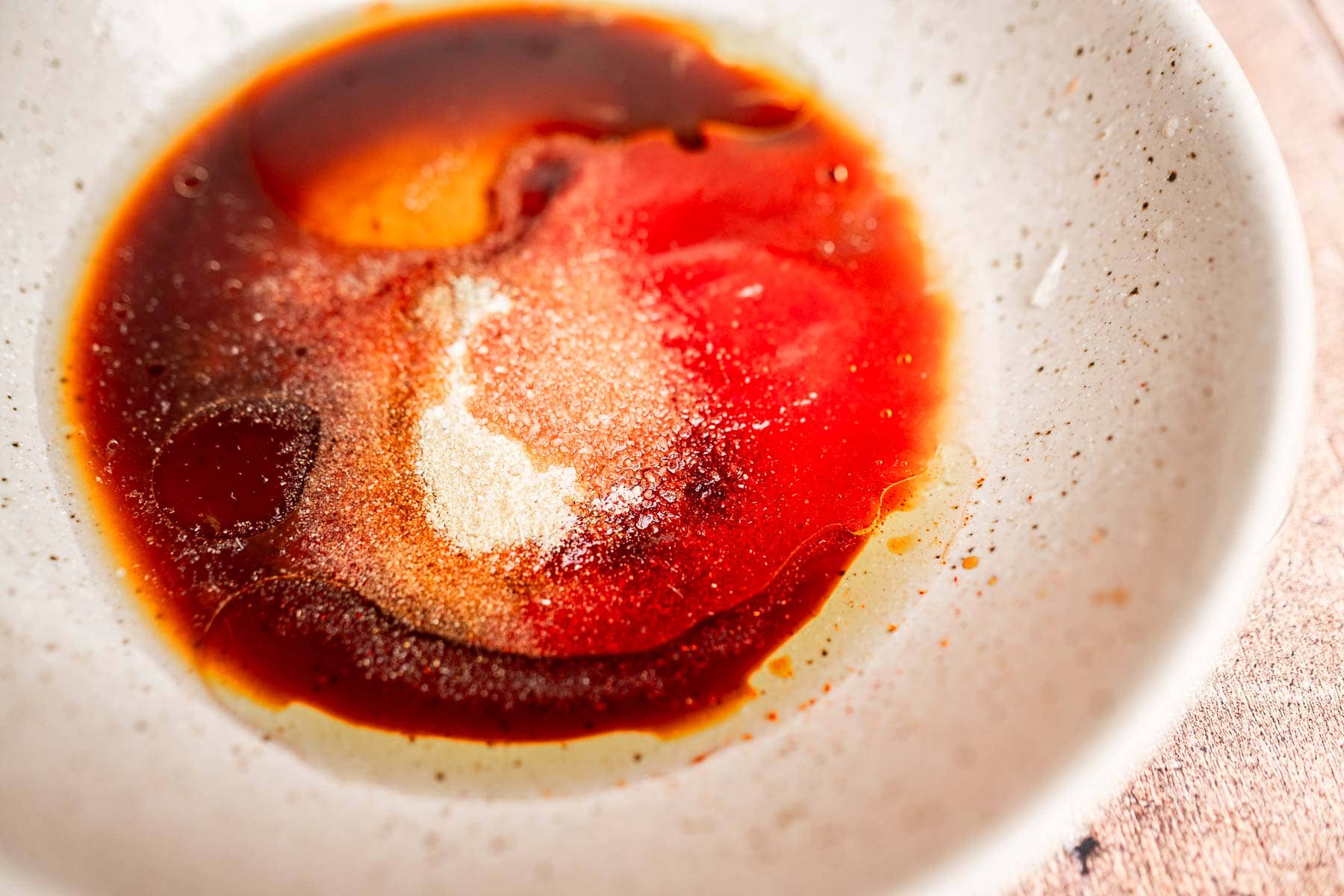 A white, speckled bowl contains a colorful blend reminiscent of tofu tacos, with a mixture of brown and red liquids and white granules sprinkled on the surface.