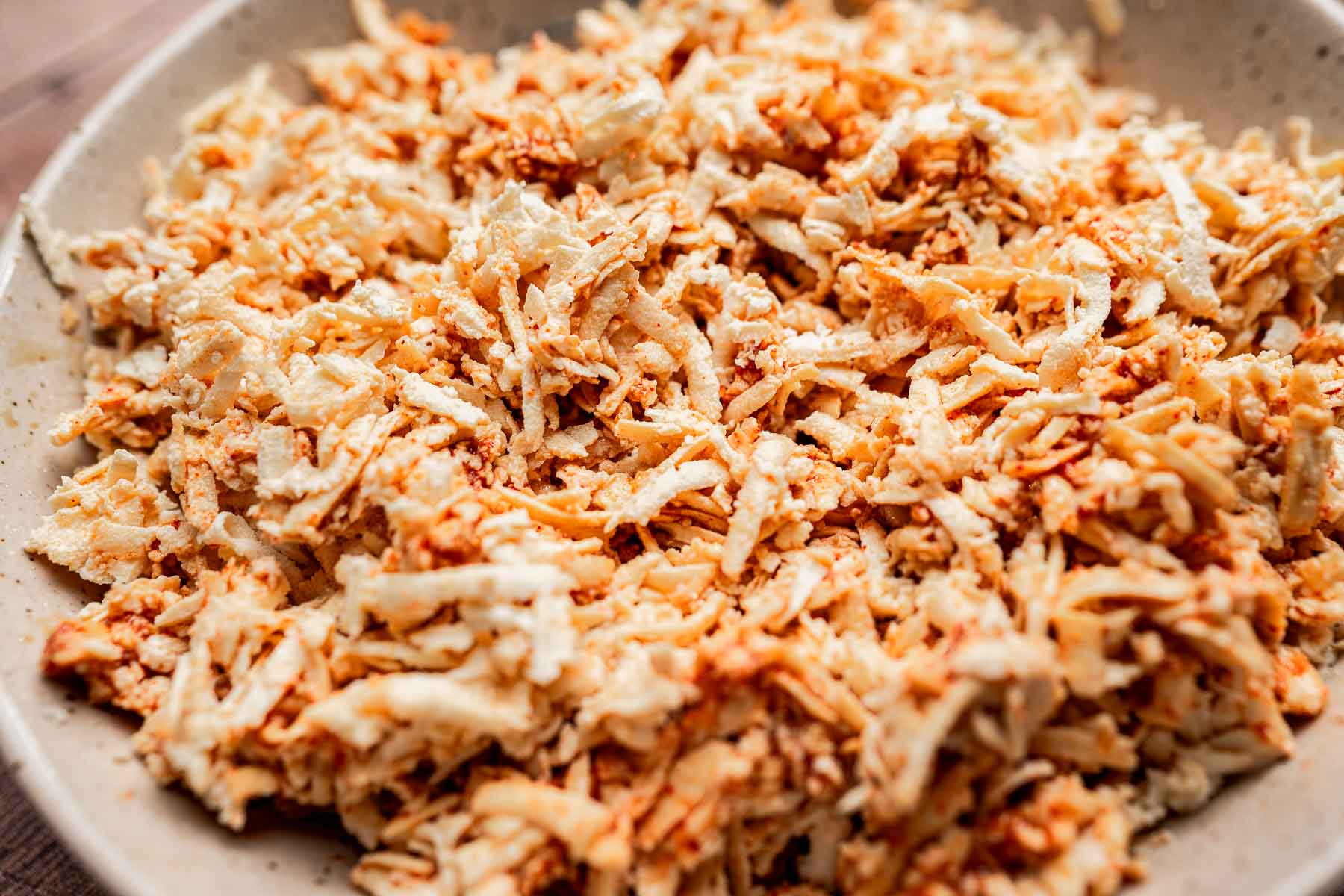 A close-up of a bowl filled with shredded jackfruit, seasoned with spices, creating a texture reminiscent of pulled meat, perfect as a filling for tofu tacos.