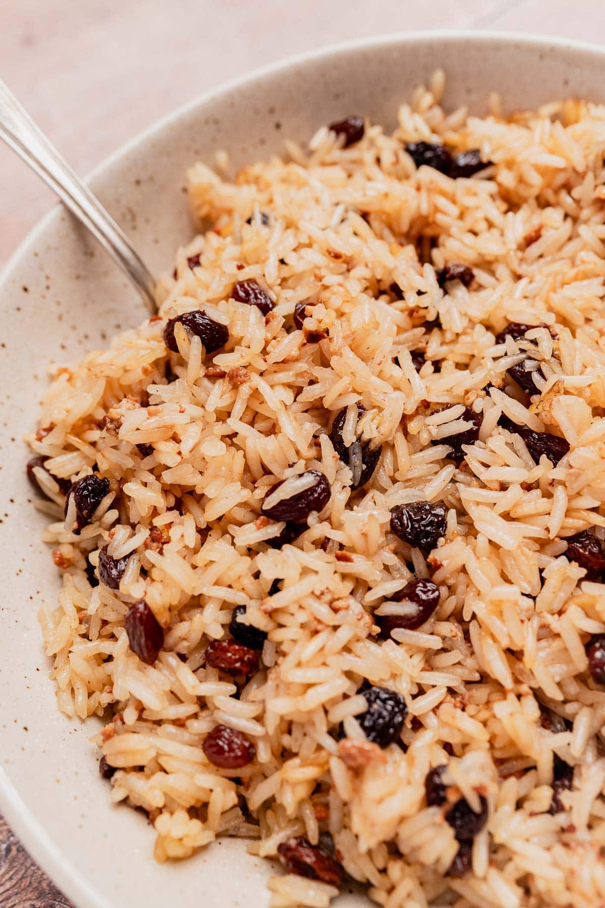A close-up of a bowl of Arroz con Coco, delicious cooked rice mixed with raisins, with a spoon resting in the bowl.