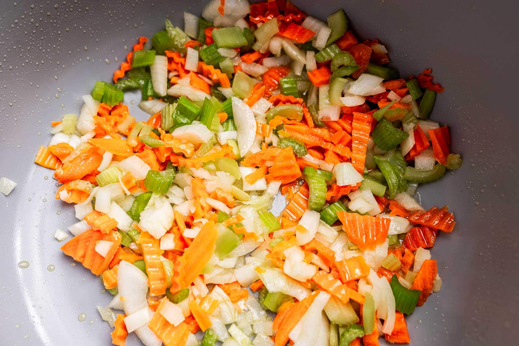 Chopped carrots, celery, and onions cooking in a pan with a small amount of oil—perfect as the flavorful base for a hearty vegetarian bolognese.