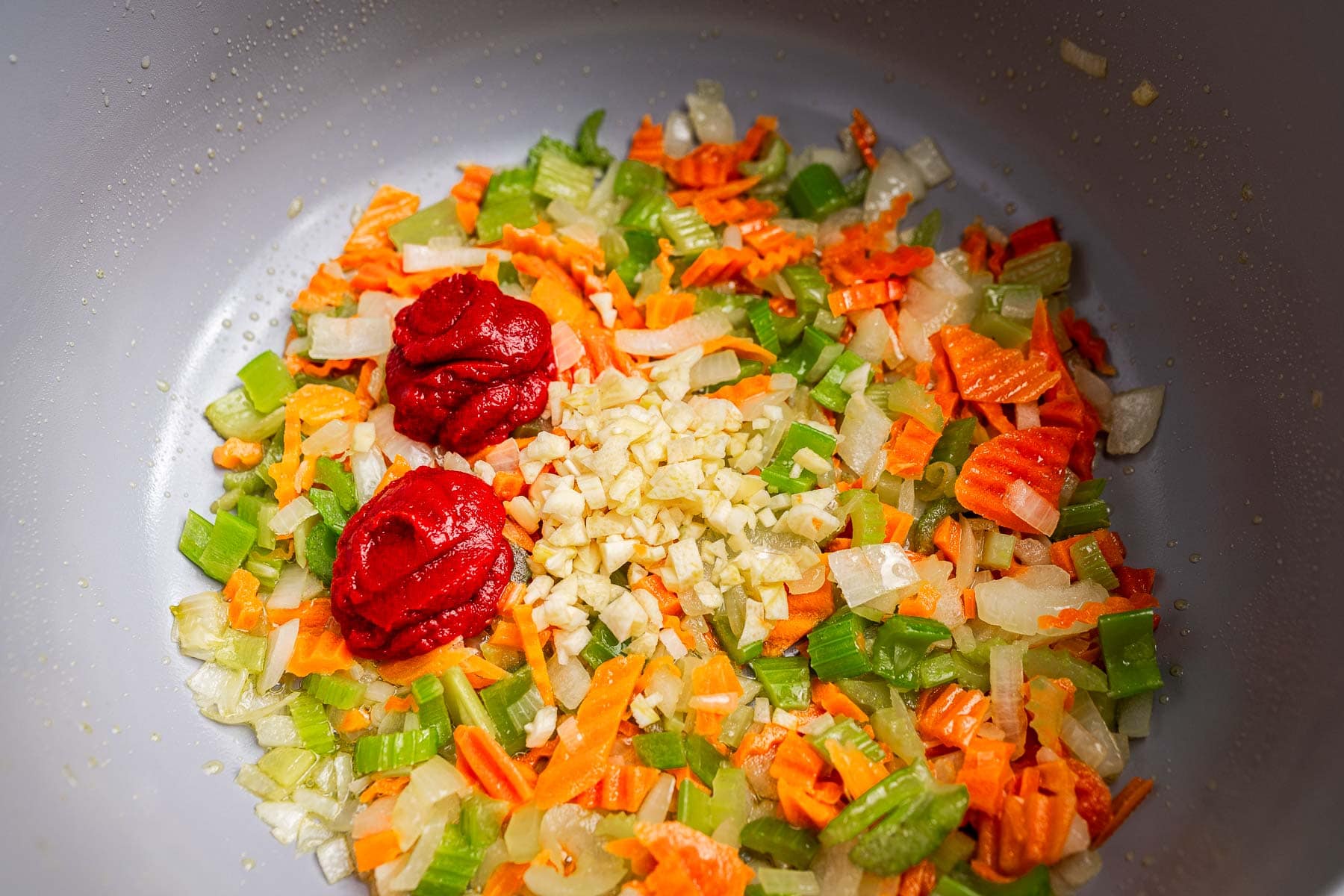 Chopped carrots, celery, and onions sauté in a pan with two dollops of tomato paste and a pile of minced garlic in the center—the flavorful base for a hearty vegetarian bolognese.