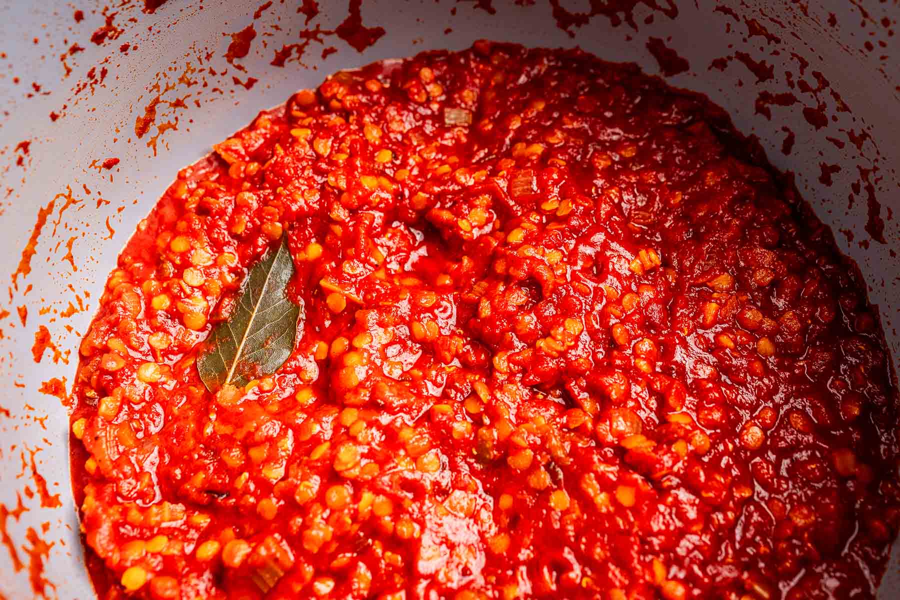 A close-up of a pot filled with thick vegetarian bolognese sauce, featuring diced onions and a bay leaf simmering in rich tomato sauce.