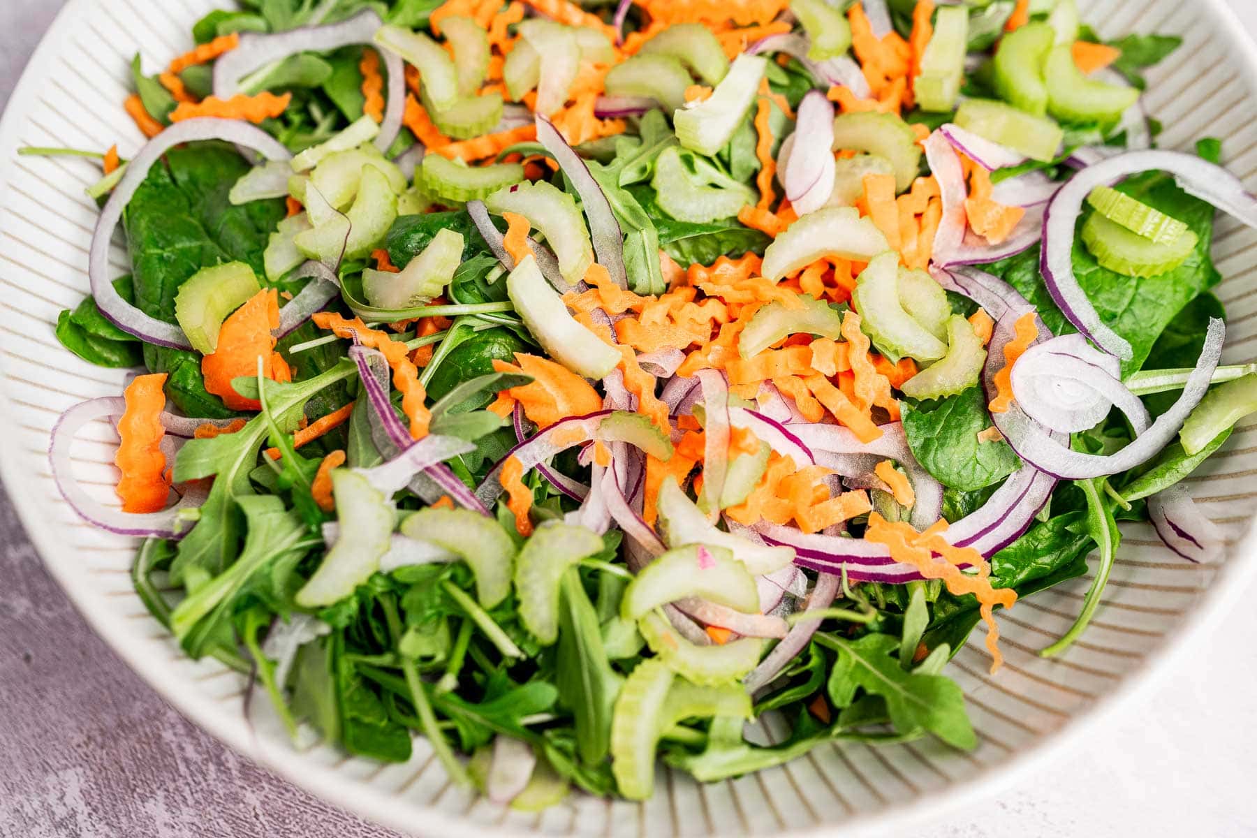 A vibrant spinach and arugula salad featuring fresh greens, sliced red onions, grated carrots, and crisp celery in every bite.