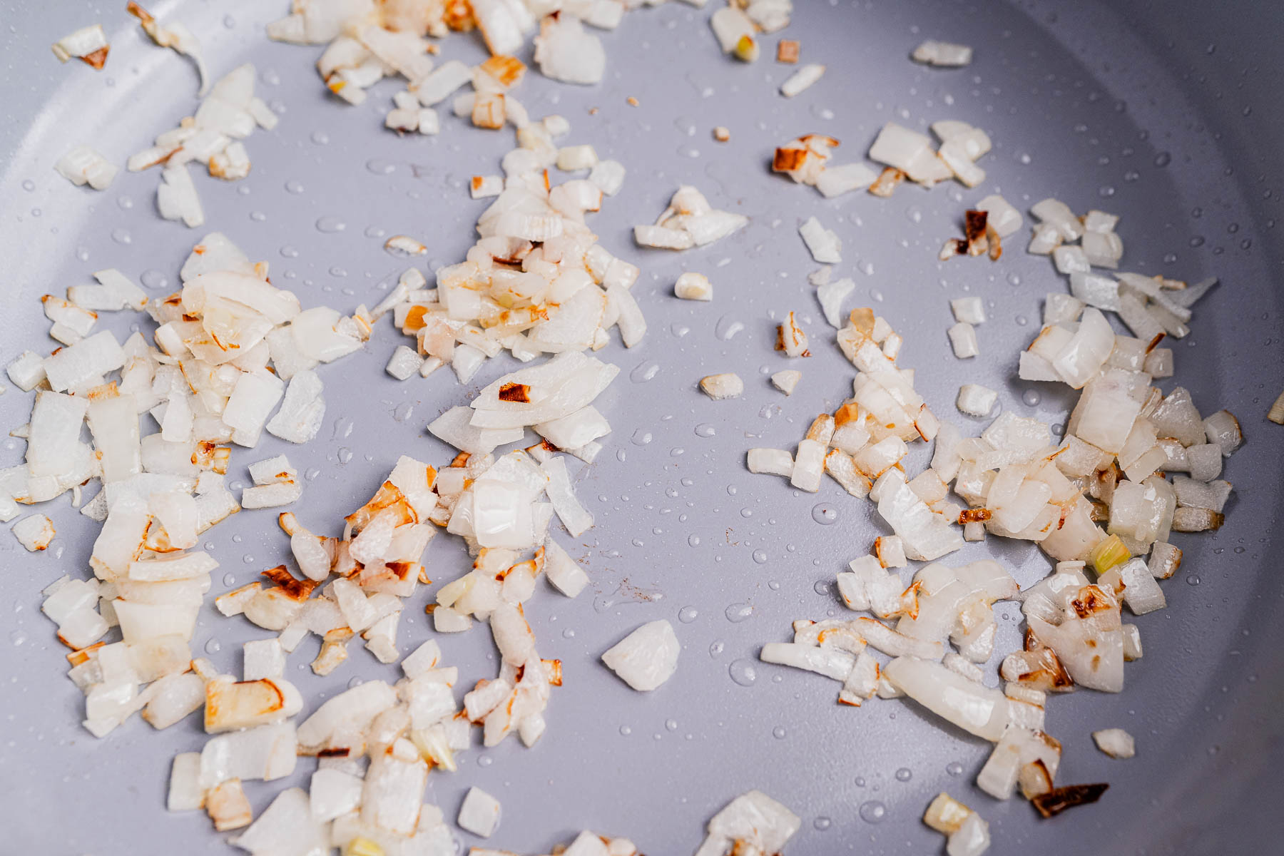 Chopped onions are being sautéed in a pan, with some pieces starting to brown and caramelize—the perfect start for a delicious ginataang langka.
