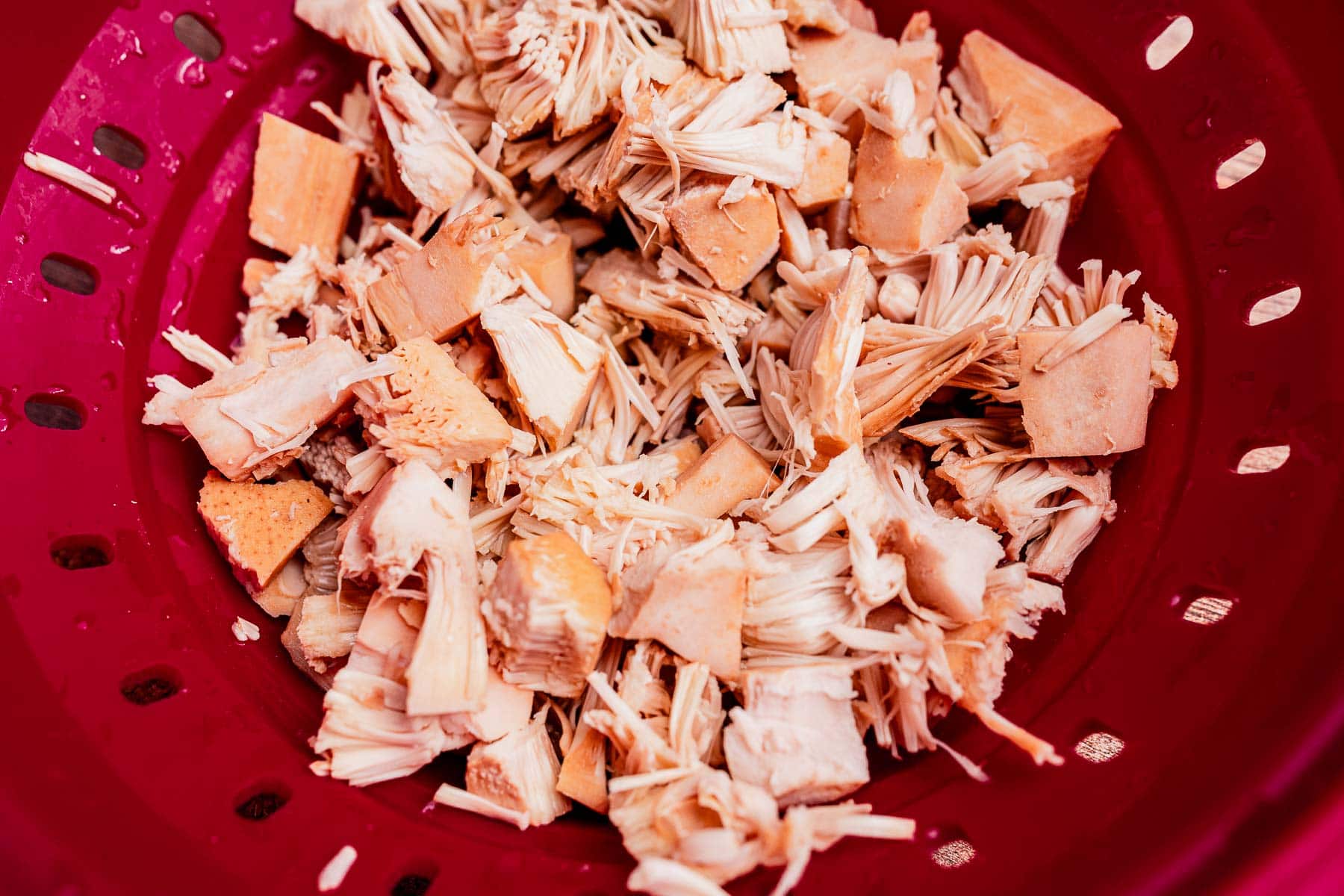 Chopped pieces of jackfruit in a red colander, perfect for making ginataang langka.