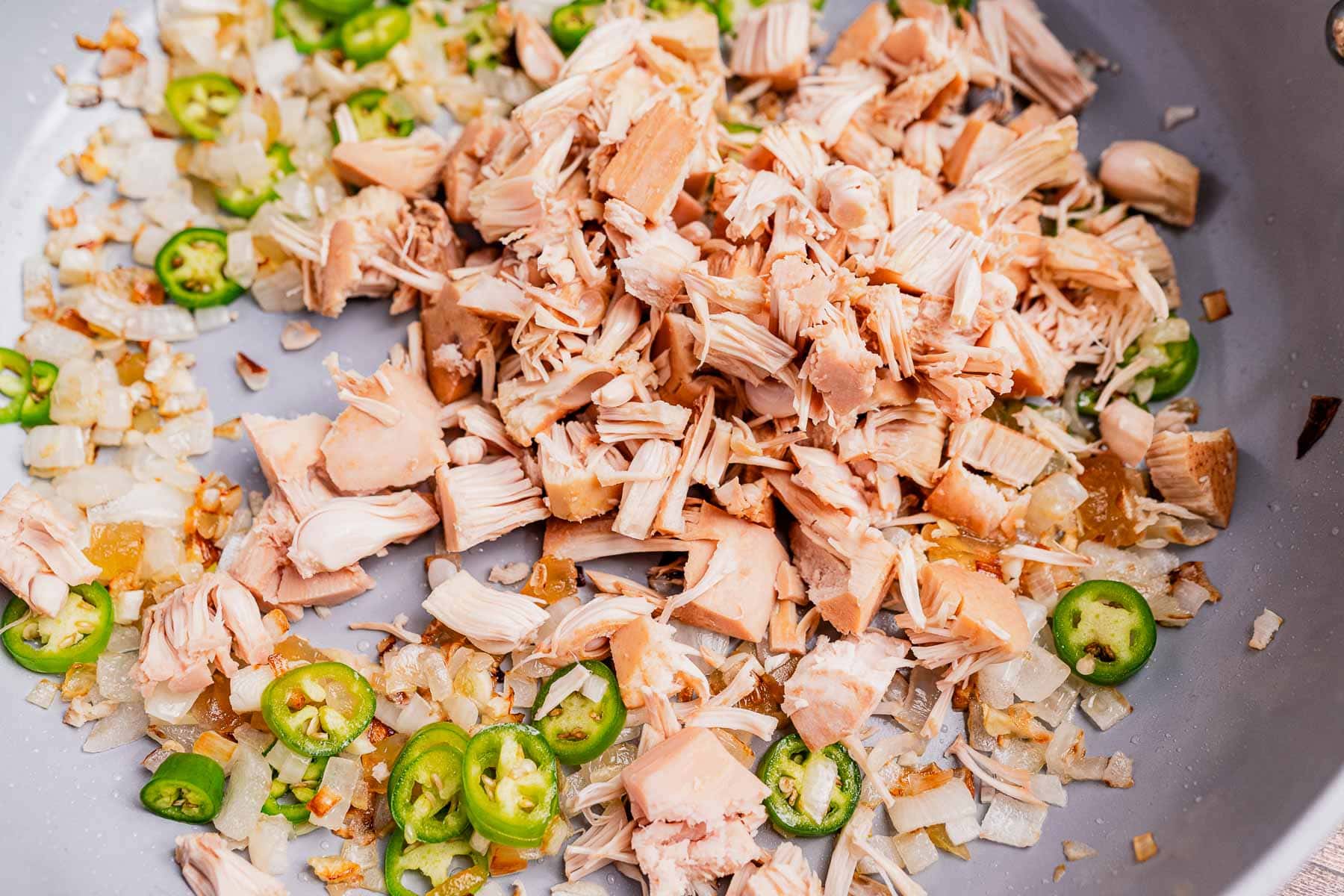 Chopped jackfruit, sliced green chilies, and diced onions simmer in a skillet, creating the base for flavorful ginataang langka.