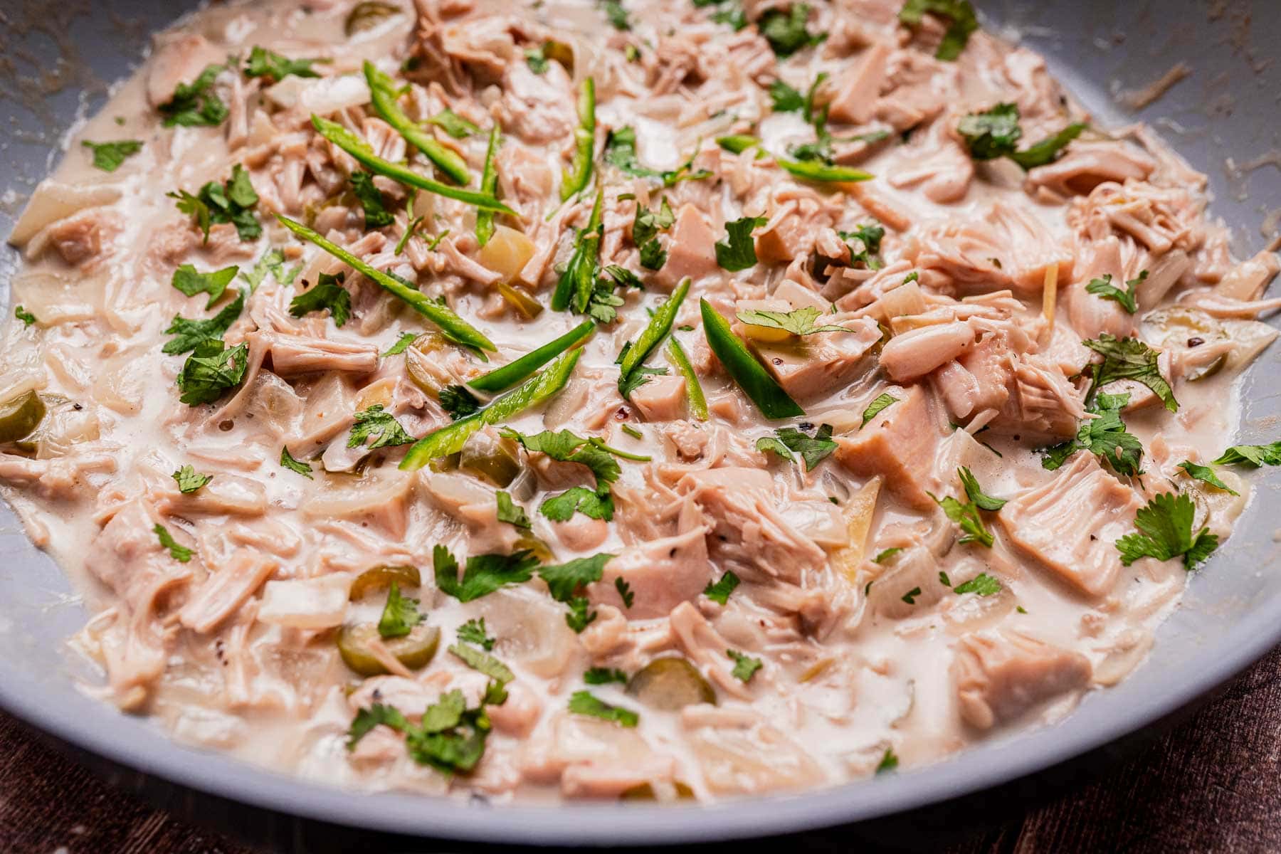 Shredded jackfruit in a creamy ginataang langka sauce, garnished with sliced green chilies and fresh cilantro, served in a shallow bowl.