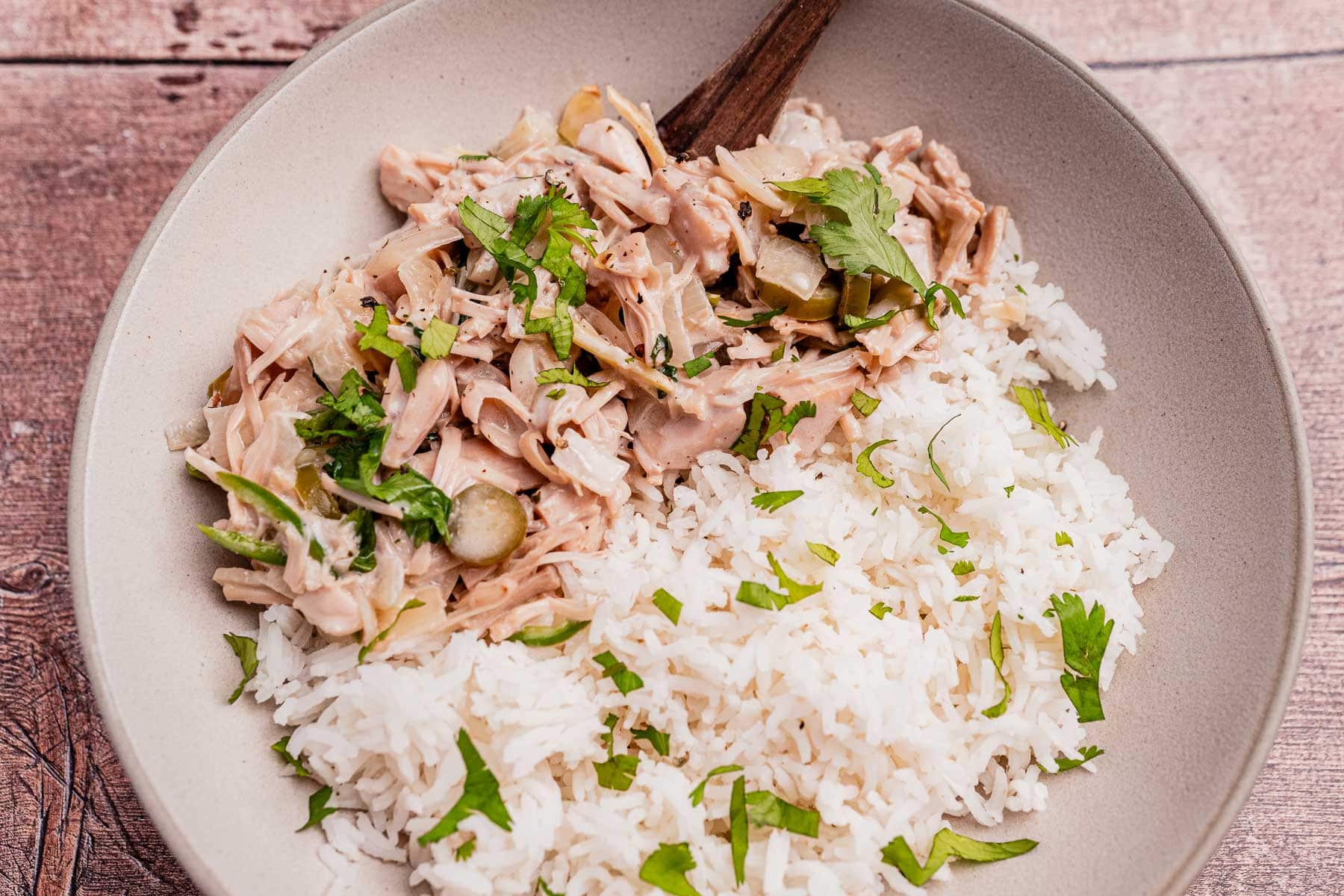 A bowl of ginataang langka—shredded jackfruit in sauce with sliced pickles and herbs—served alongside white rice and garnished with fresh cilantro.