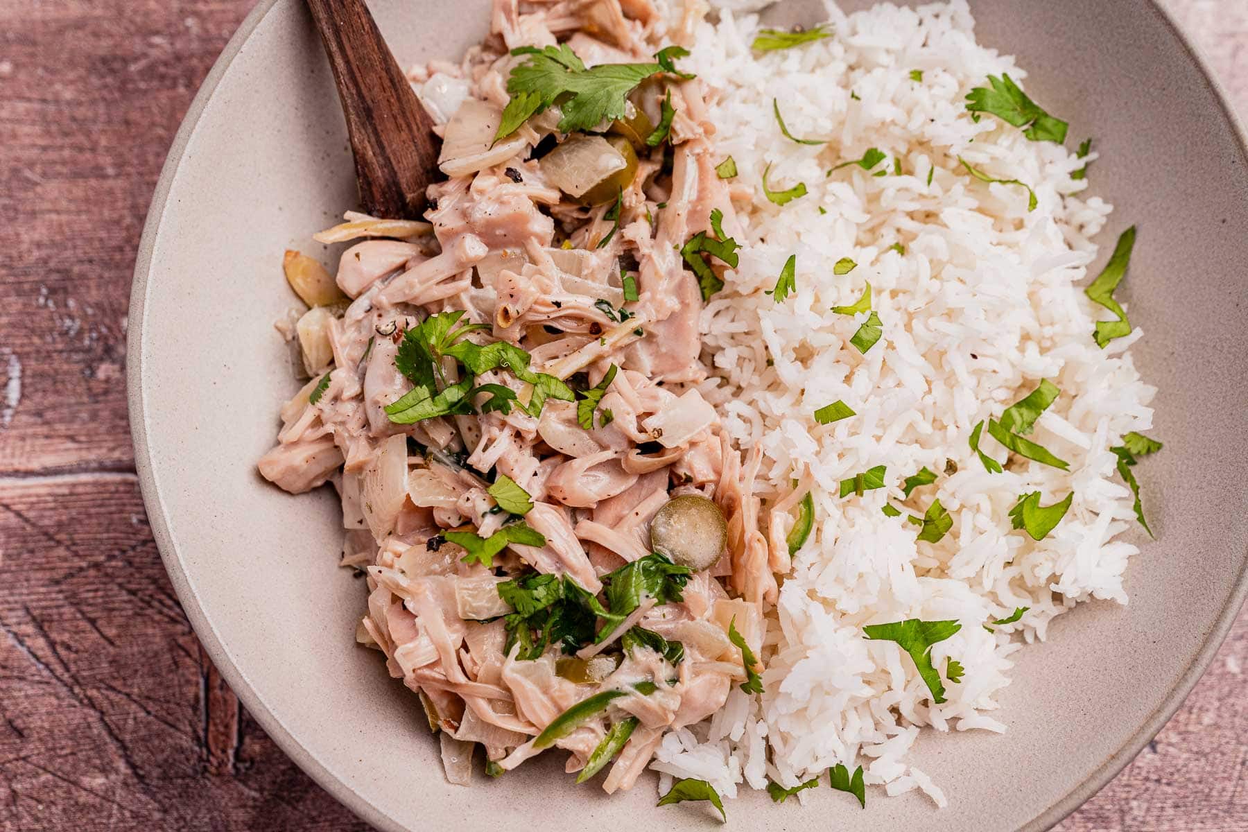 A plate with white rice and ginataang langka—shredded jackfruit simmered in a savory coconut sauce—garnished with chopped cilantro.