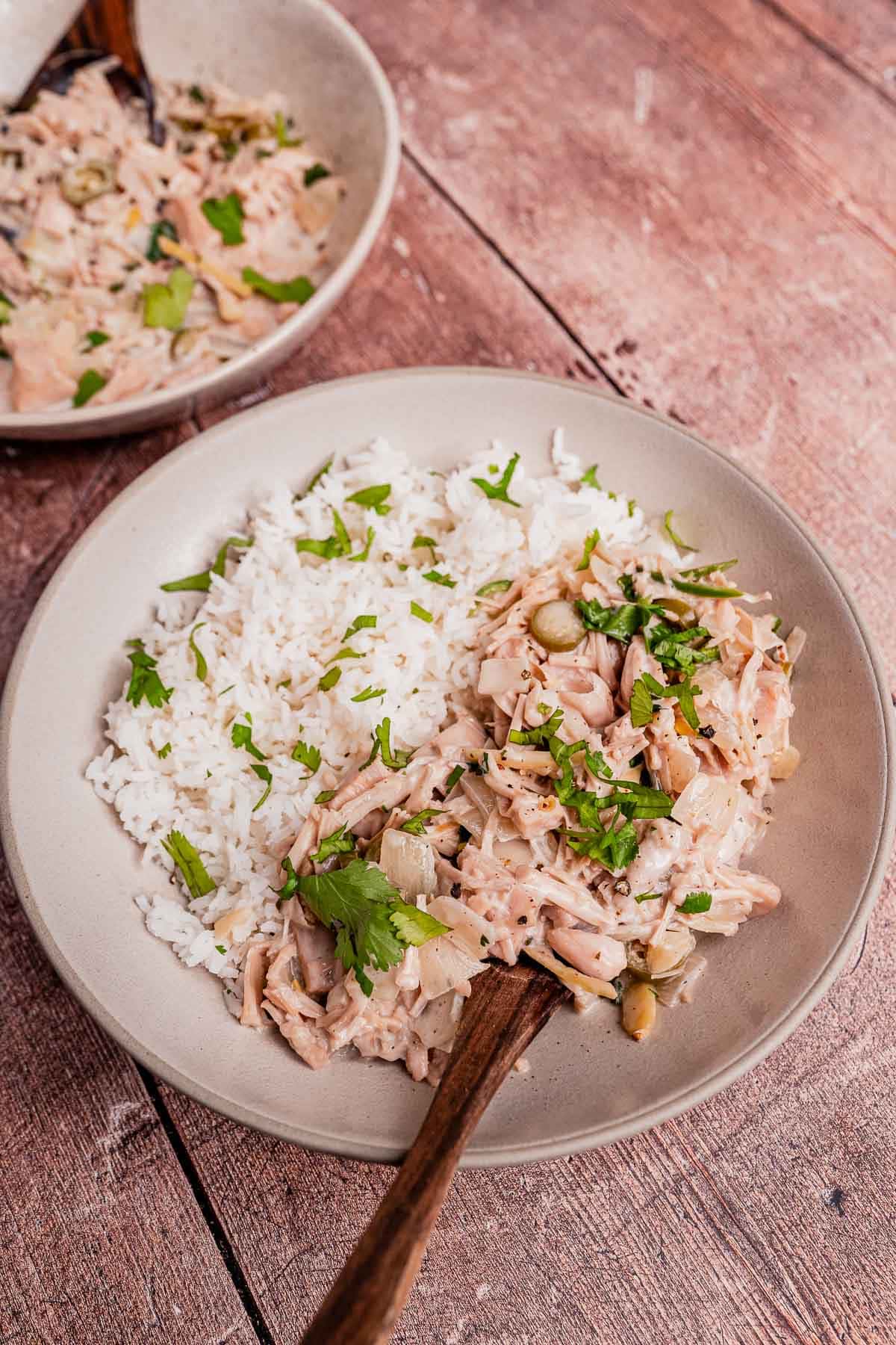 A plate with white rice and shredded chicken in a creamy ginataang langka sauce, garnished with chopped herbs, on a wooden table.