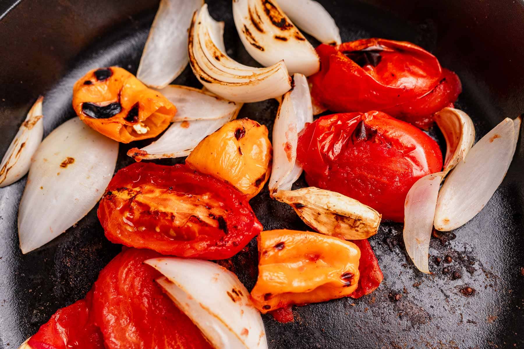 Charred tomatoes, onions, and yellow peppers in a skillet, showing grill marks and slight caramelization—perfect for blending into a zesty habanero salsa.