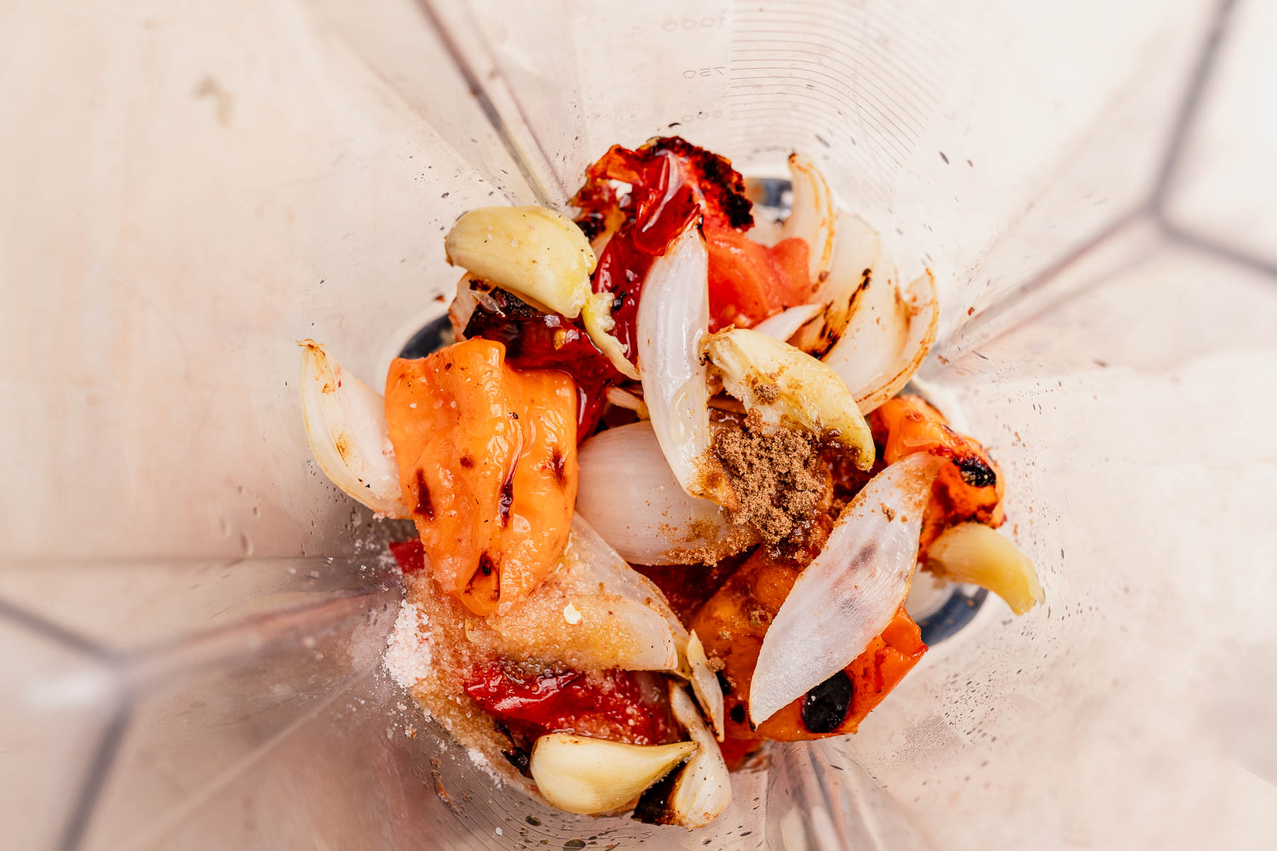 Charred tomatoes, onions, garlic, and spices with salt are blended together to create a vibrant habanero salsa, viewed from above.
