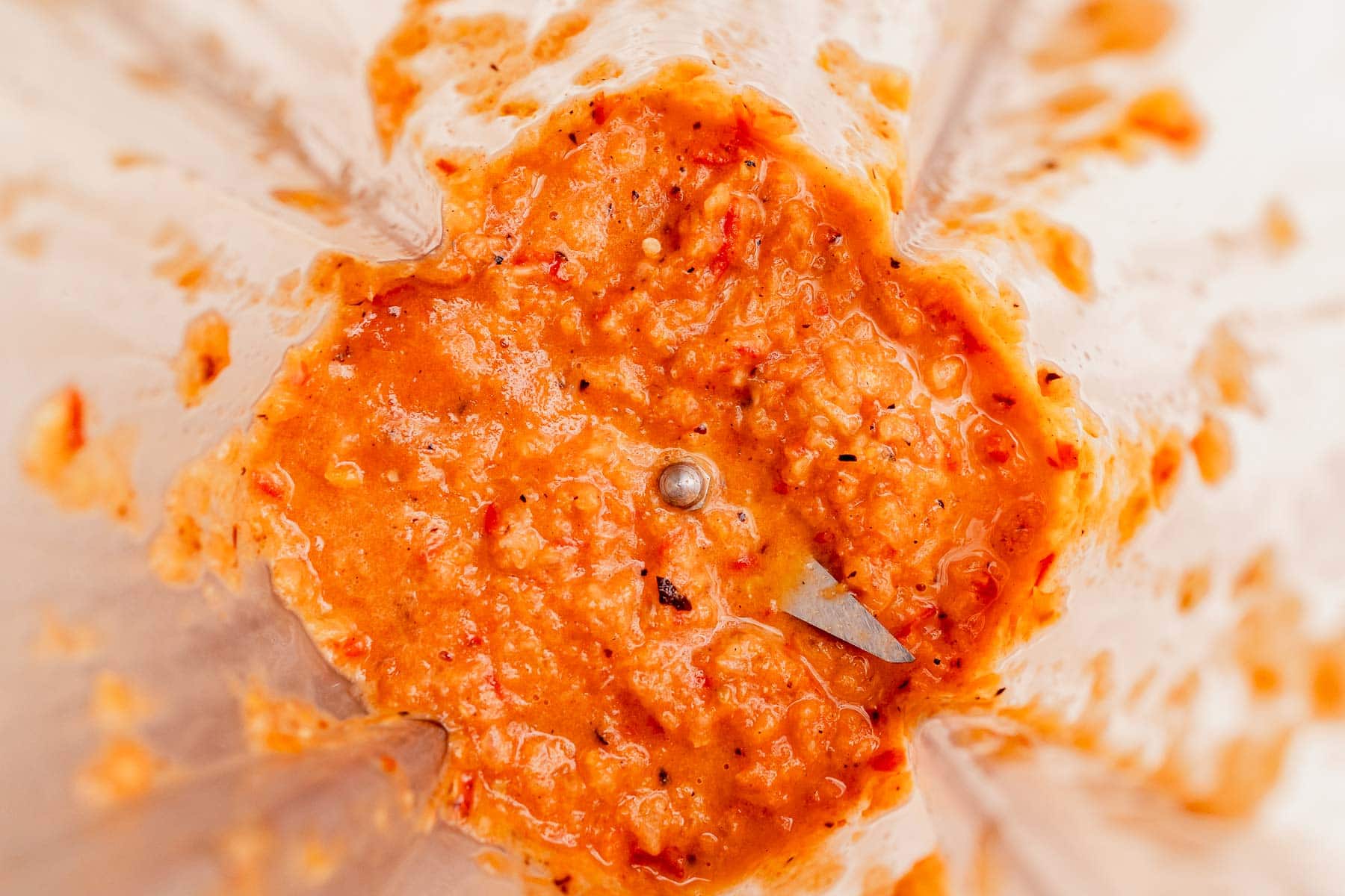 Orange-red chunky habanero salsa mixture inside a blender, viewed from above, with visible metal blender blade and food splatters on the sides.
