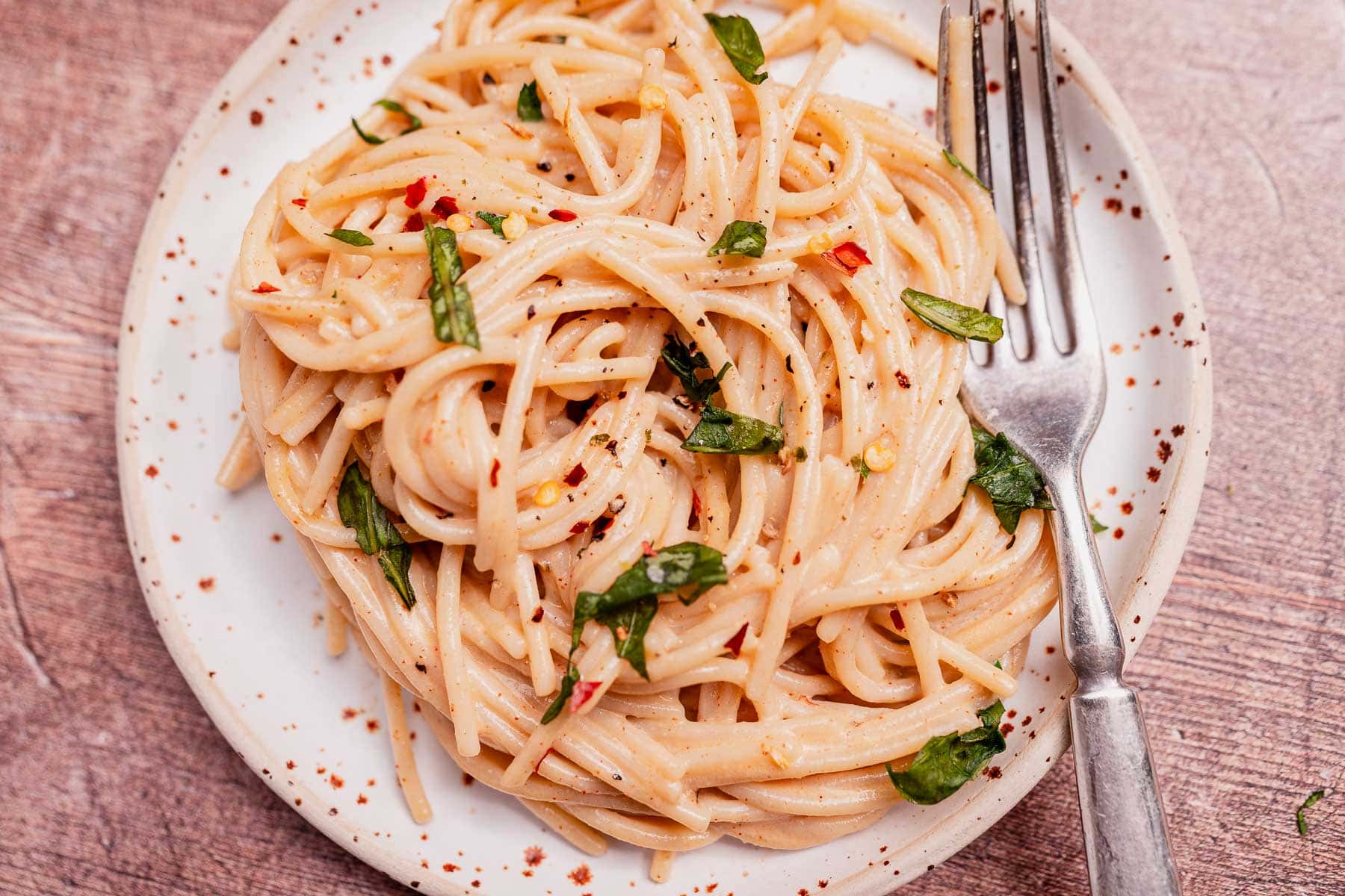 A plate of spaghetti with a creamy coconut milk pasta sauce, garnished with fresh herbs and red pepper flakes, with a fork resting on the plate.