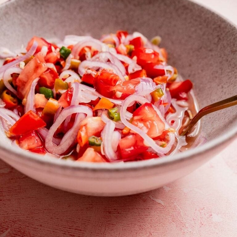 A bowl of sambal dabu dabu-style tomato and onion salad with sliced green chilies and a light dressing, served with a spoon.