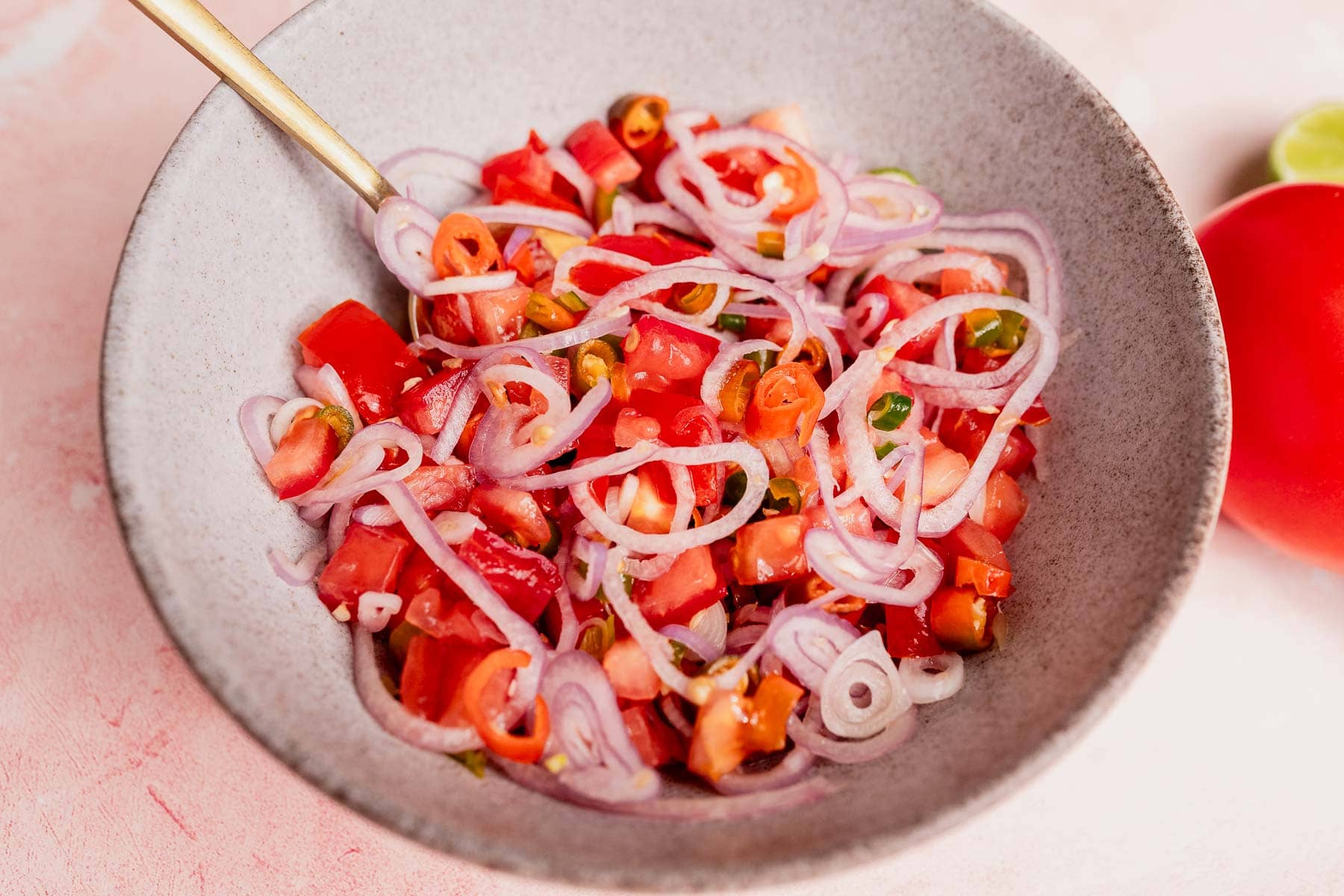 A bowl of chopped tomatoes, sliced red onions, and diced green chilies—classic ingredients for sambal dabu dabu—with a fork resting on the edge.