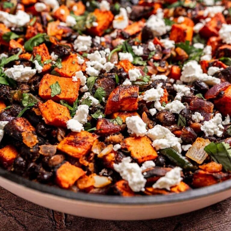 A close-up of sweet potato hash featuring roasted sweet potatoes, black beans, onions, fresh herbs, and crumbled feta cheese.