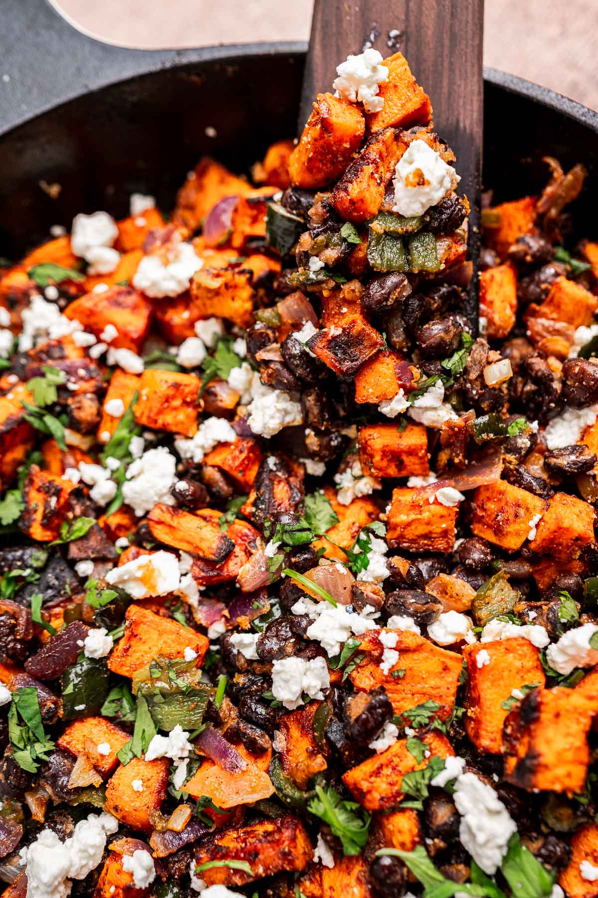 A skillet filled with sweet potato hash—roasted sweet potatoes, black beans, chopped vegetables, fresh herbs, and crumbled feta cheese.