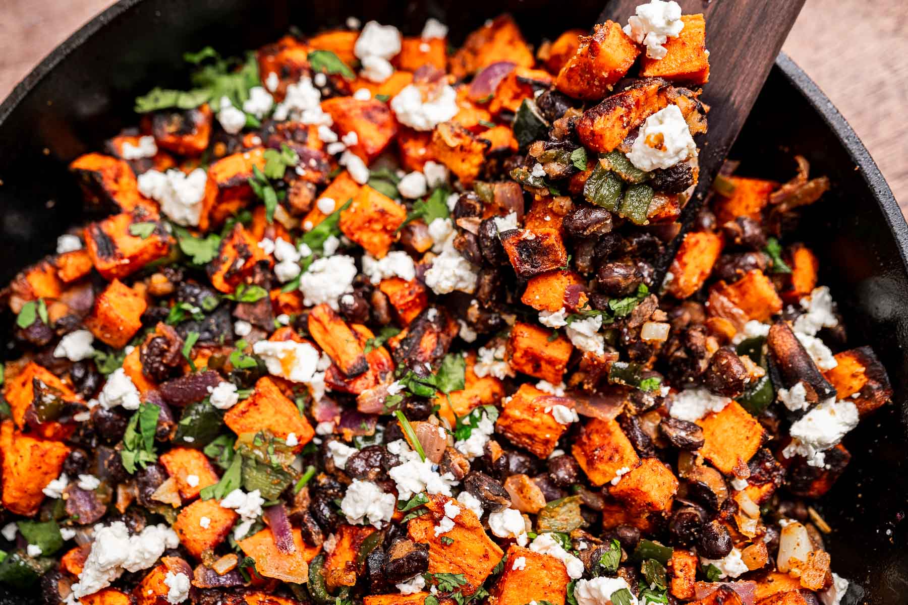 A skillet filled with sweet potato hash—roasted sweet potatoes, black beans, onions, herbs, and crumbled white cheese—for a hearty and flavorful dish.