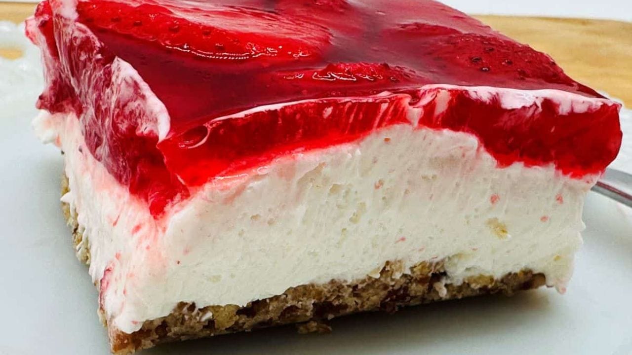 Slice of strawberry pretzel dessert with a layer of strawberries in gelatin, cream cheese filling, and crunchy pretzel crust on a white plate.
