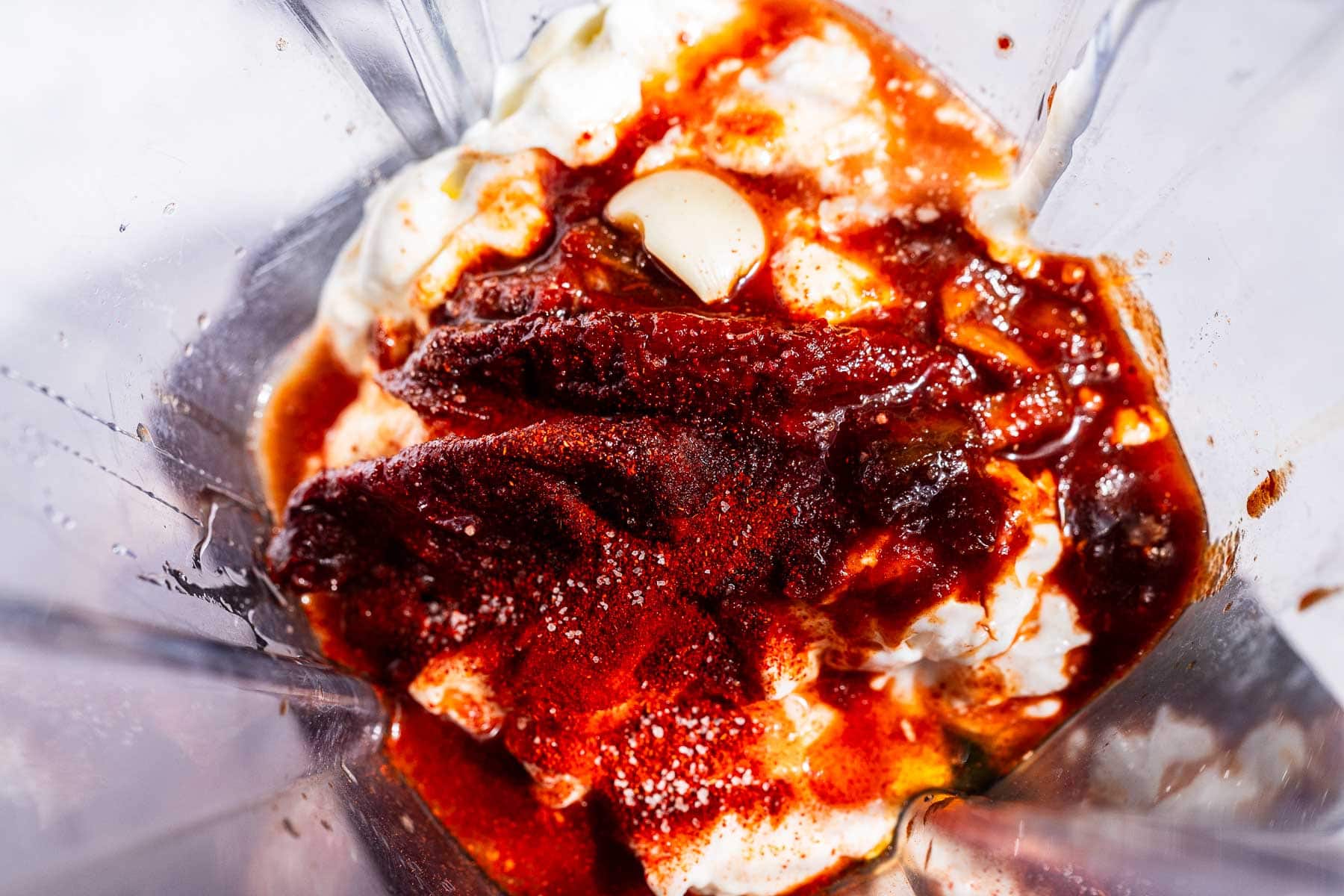 Top view of a blender with yogurt, chipotle peppers in adobo sauce, garlic, and spices—everything you need to make a creamy homemade chipotle sauce.