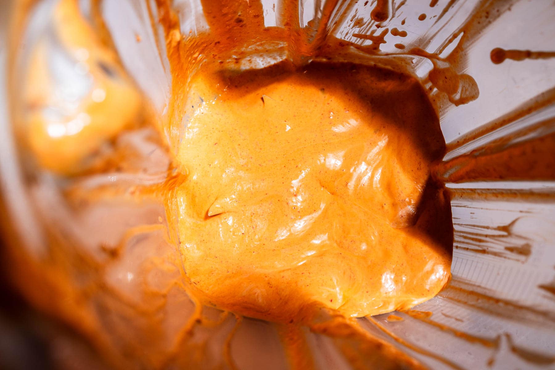 Close-up view of creamy orange chipotle sauce being blended inside a blender, with the zesty sauce splattered on the blender walls.