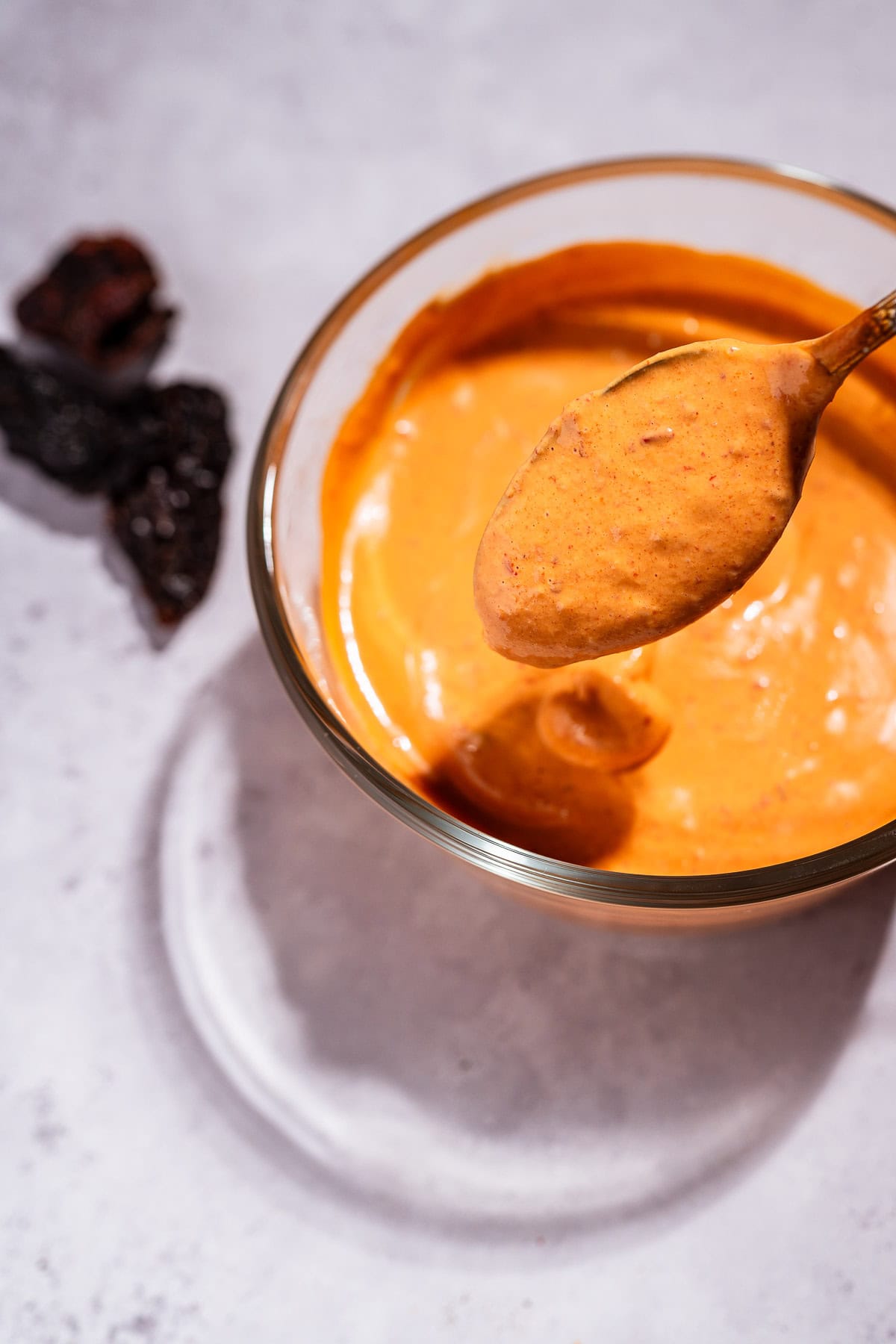 A bowl of creamy chipotle sauce with a spoonful lifted above it; dried chipotle peppers are on the side.