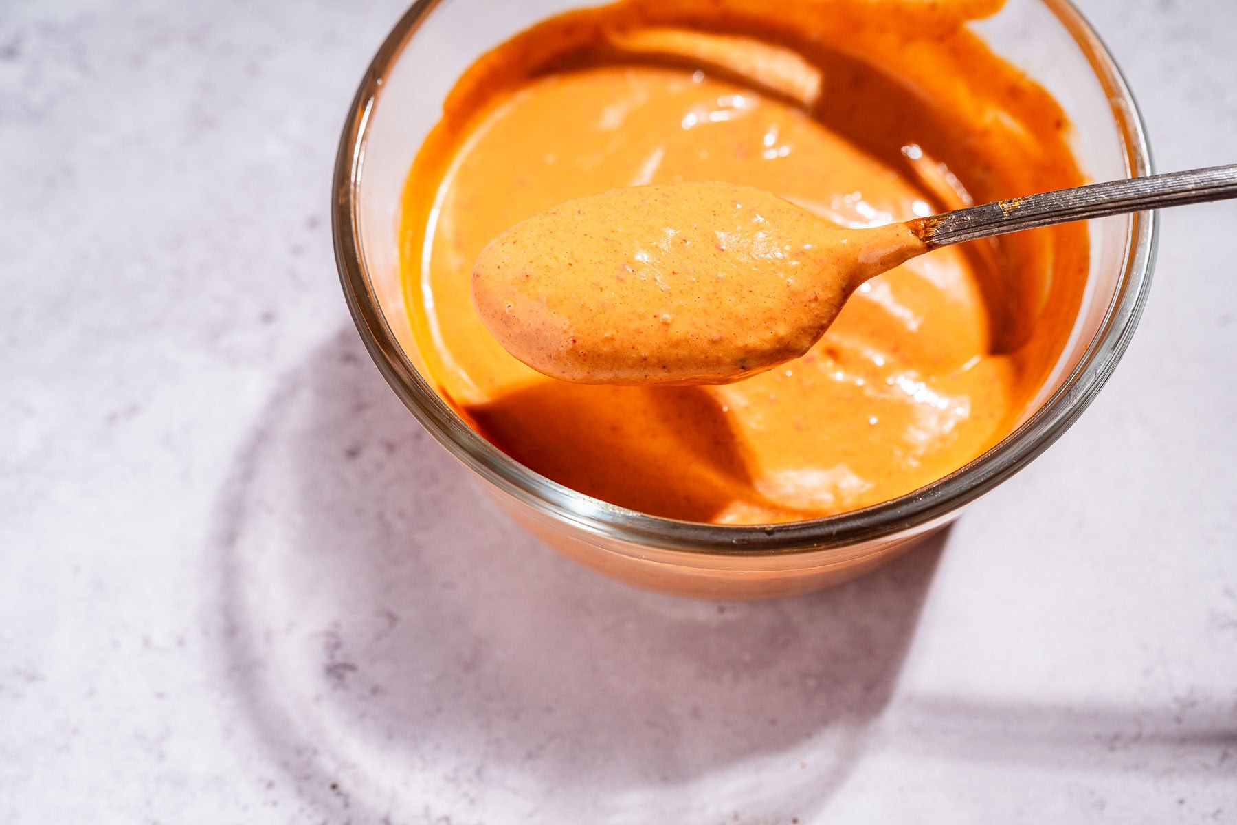 A glass bowl filled with creamy chipotle sauce, with a spoon lifting a portion of the smoky orange sauce above the bowl.