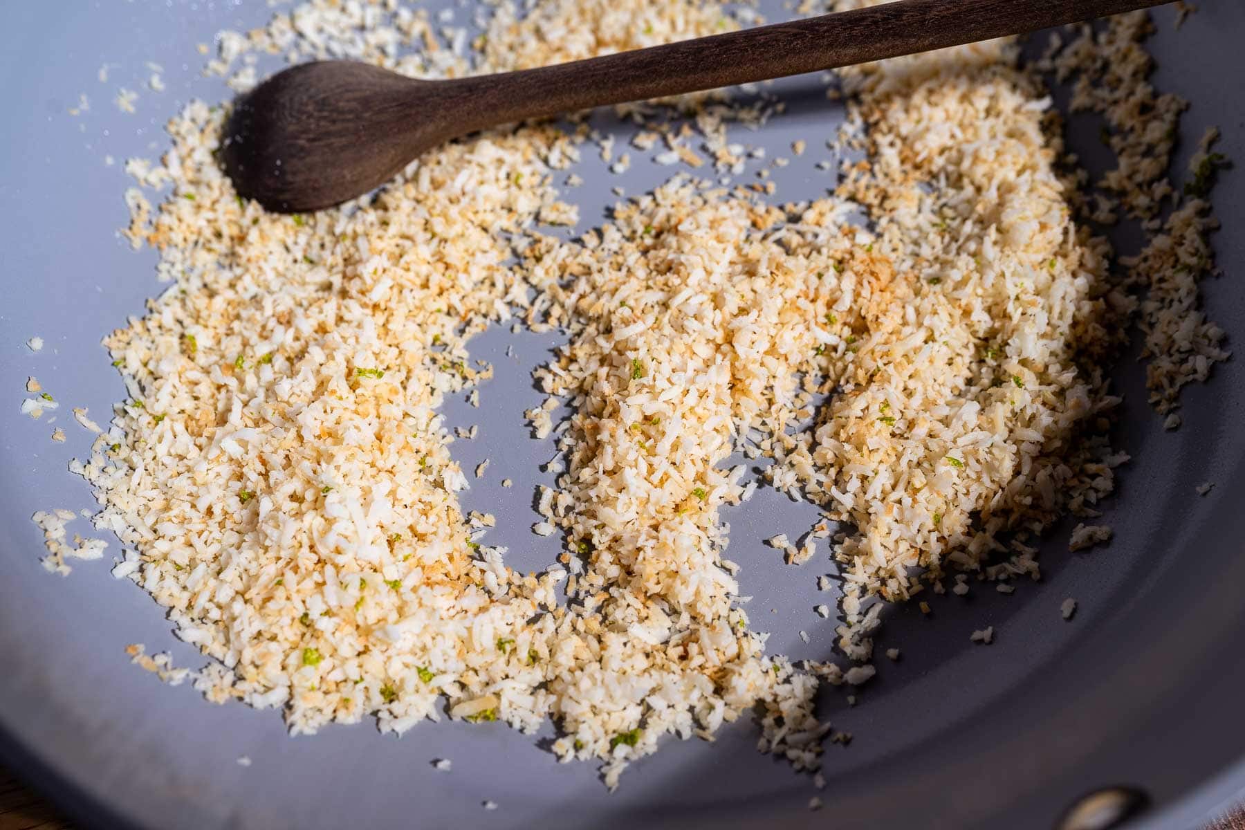 Toasted shredded coconut with a wooden spoon in a gray skillet adds a delightful crunch and flavor to any fiesta salad.
