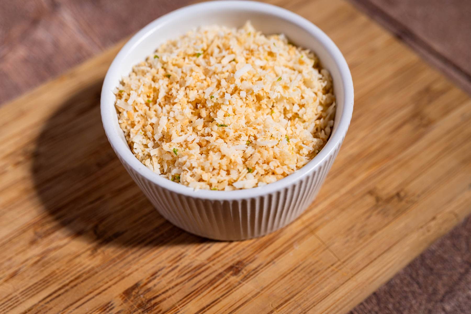A white ramekin filled with panko breadcrumbs sits on a wooden cutting board, ready to add the perfect crunch to your next fiesta salad.