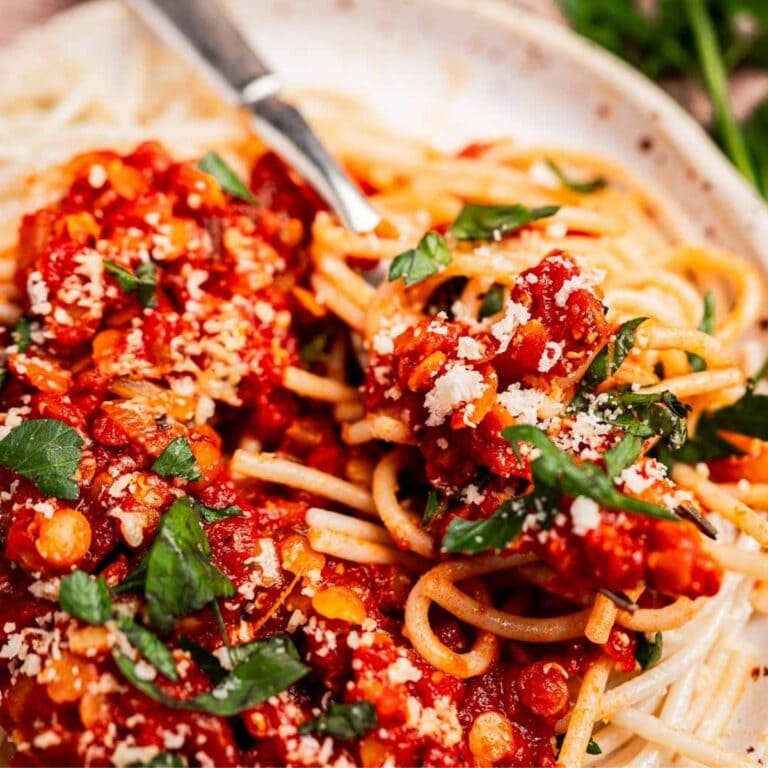 A perfect choice for vegetarian weeknight dinners, this plate of spaghetti is topped with tomato sauce, chopped parsley, and grated cheese, with a fork resting on the side.
