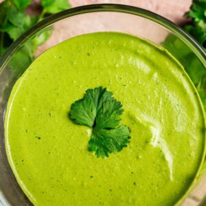 A glass bowl filled with creamy green cilantro sauce, garnished with two cilantro leaves on top.