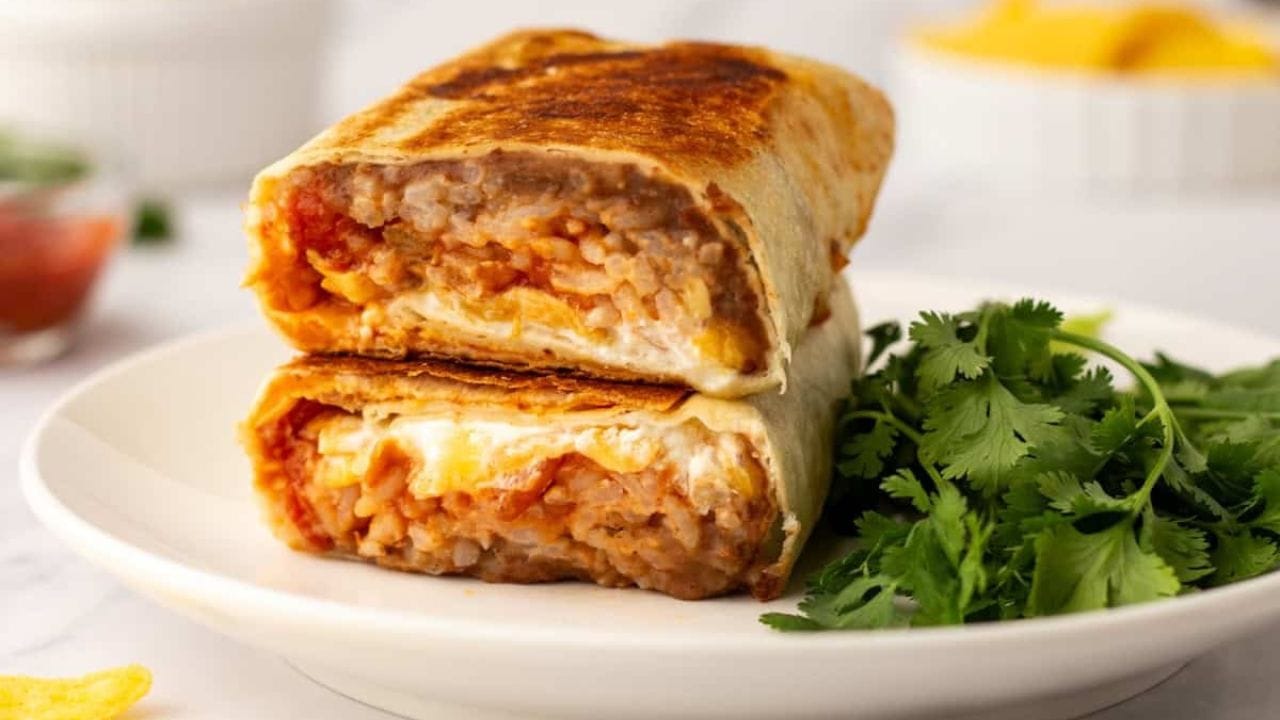 A close up image of cheesy bean and rice burrito on a plate.