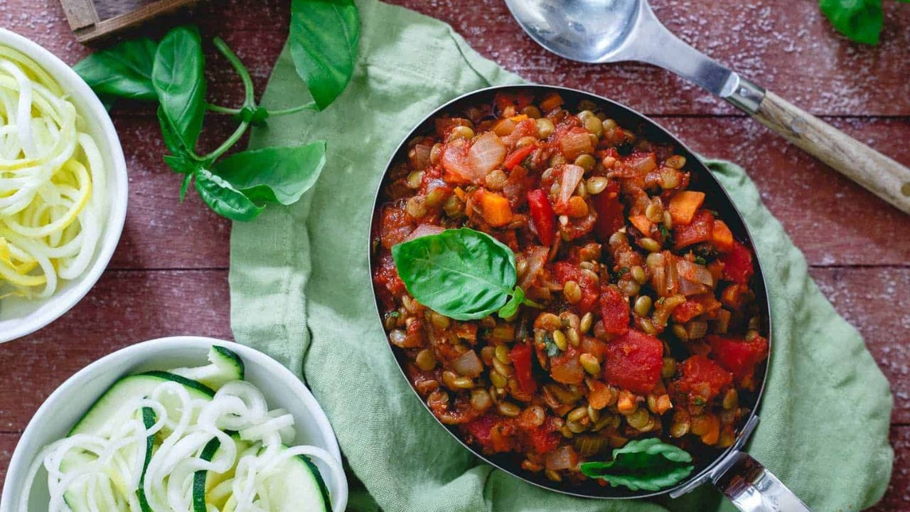 Lentil bolognese garnished with basil in a metal dish.