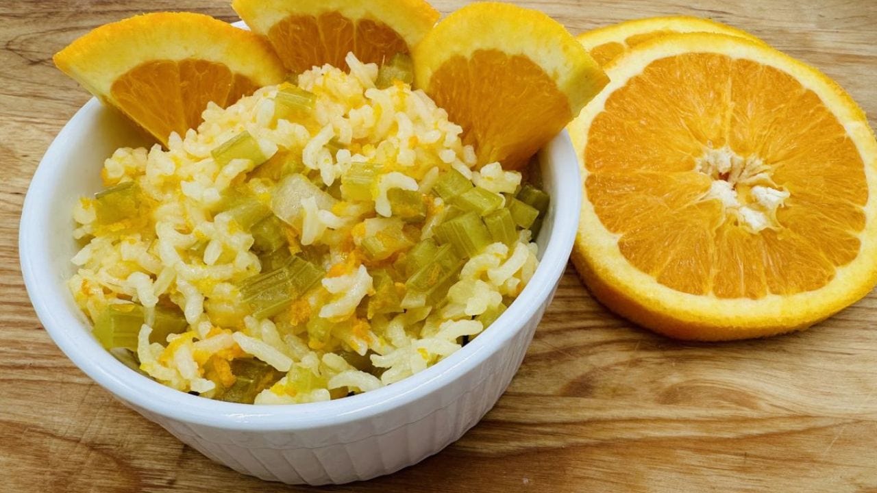 Bowl of rice with chopped celery and orange slices on a wooden table.