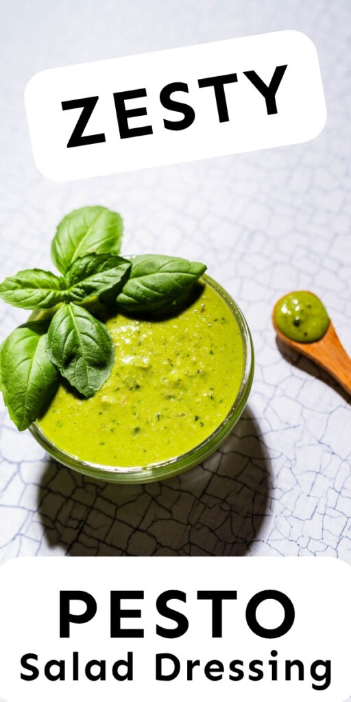 A bowl of pesto salad dressing garnished with fresh basil leaves sits on a cracked white surface, with a spoonful beside it. Text reads "Zesty Pesto Salad Dressing.