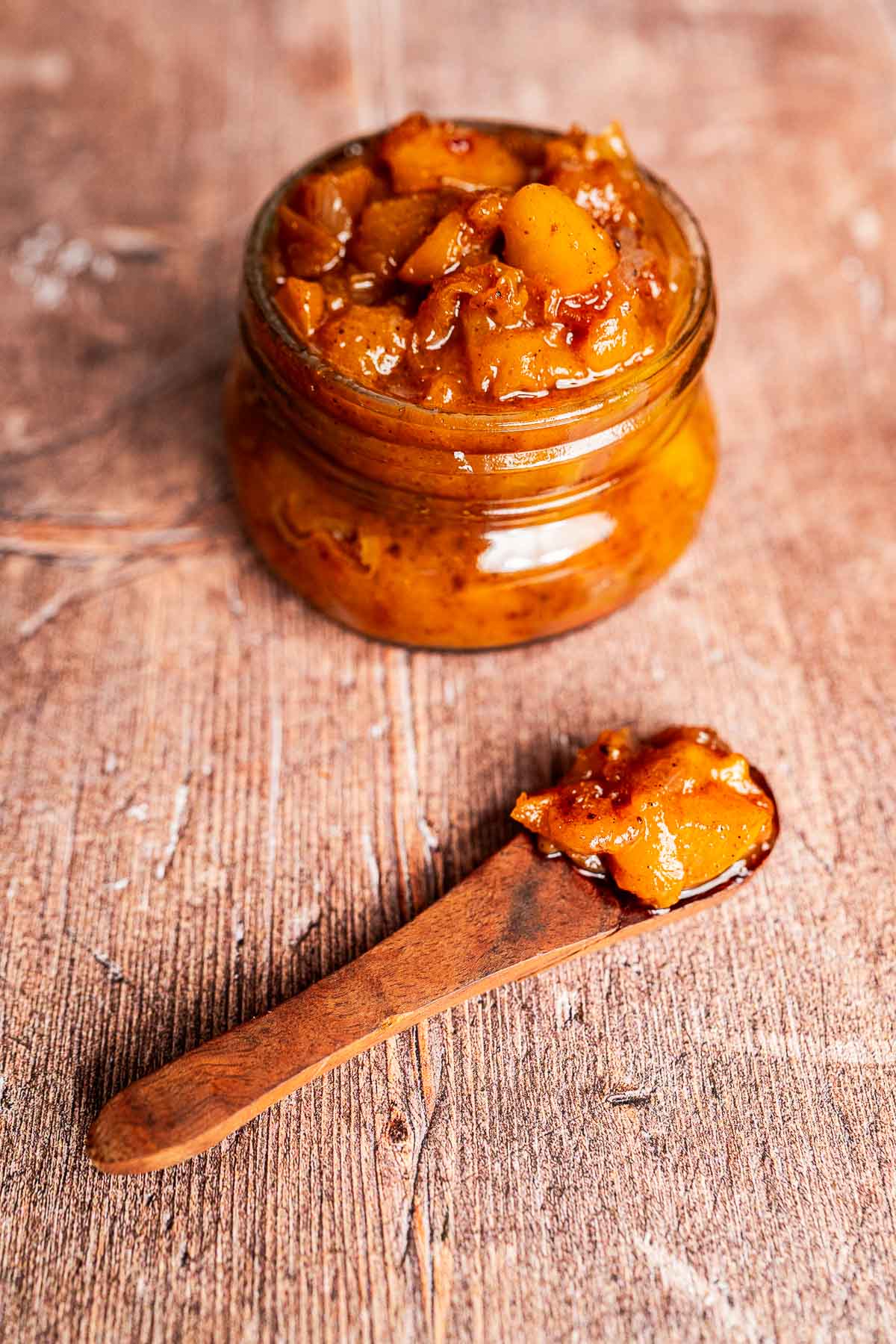 Golden peach chutney in a glass jar with warm wooden backdrop.