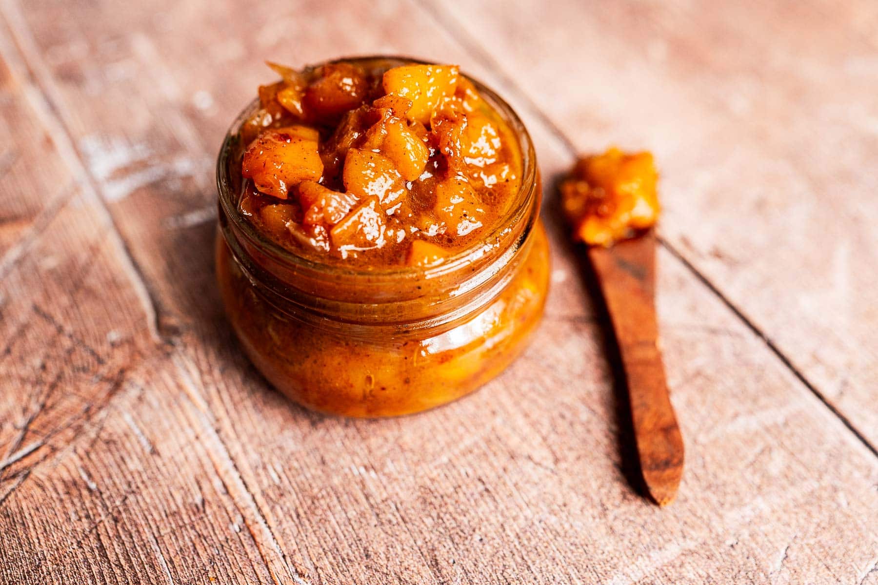 Overhead view of chunky peach chutney with a wooden spoon.
