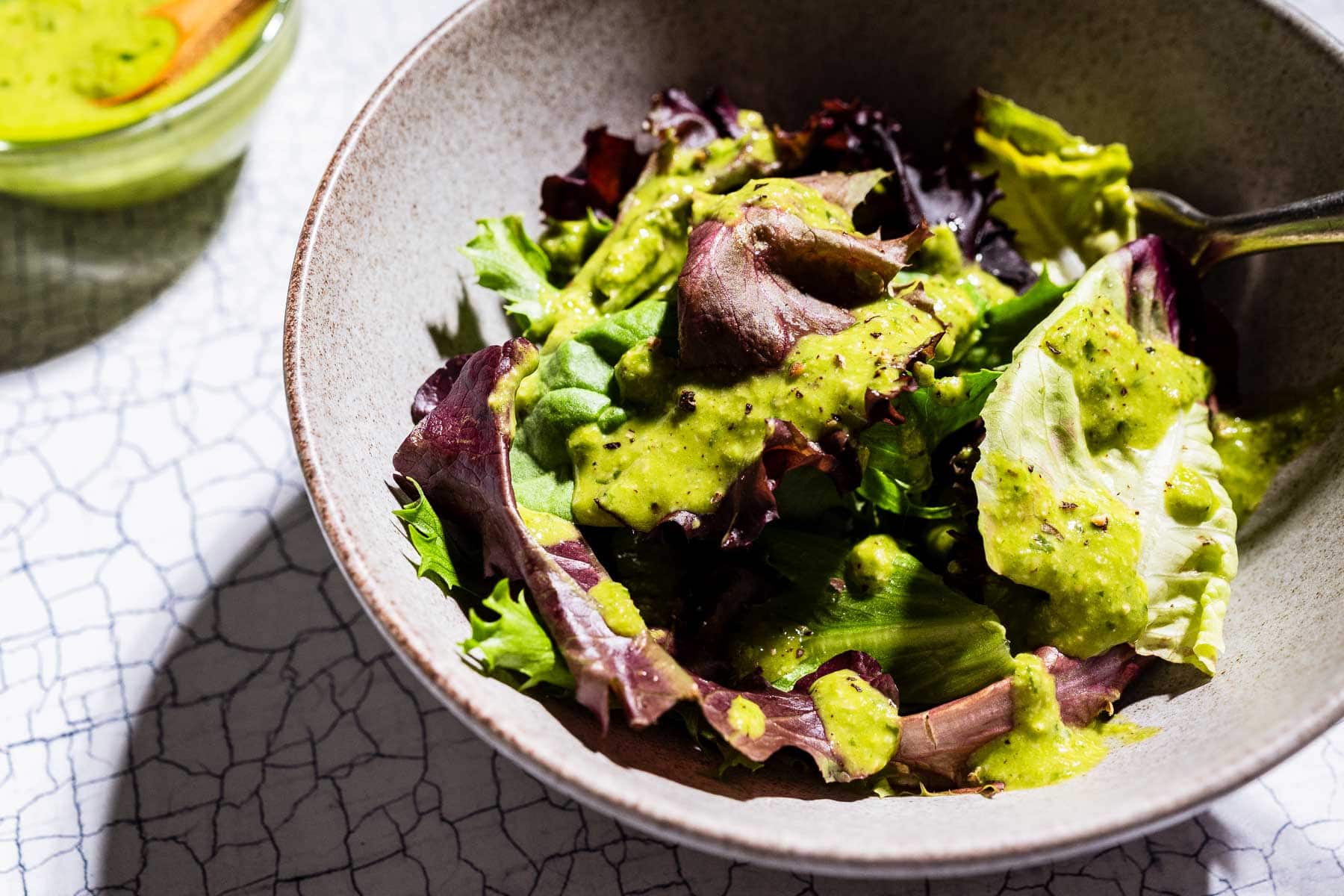A bowl of mixed leafy greens topped with a vibrant pesto salad dressing, with a fork resting inside the bowl.