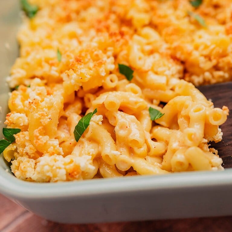 Close-up of gluten free mac and cheese topped with golden breadcrumbs and garnished with small green herb leaves in a baking dish.